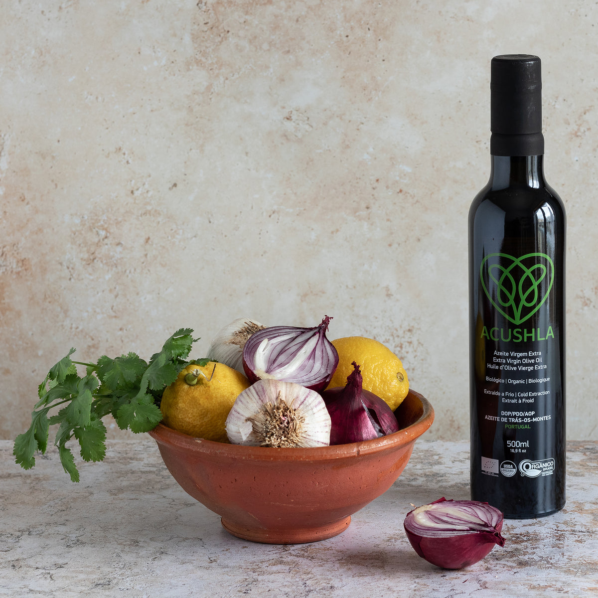 Acushla Organic DOP Trás-os-Montes 500 ml bottle beside a bowl of onions, garlic, lemons, and cilantro.