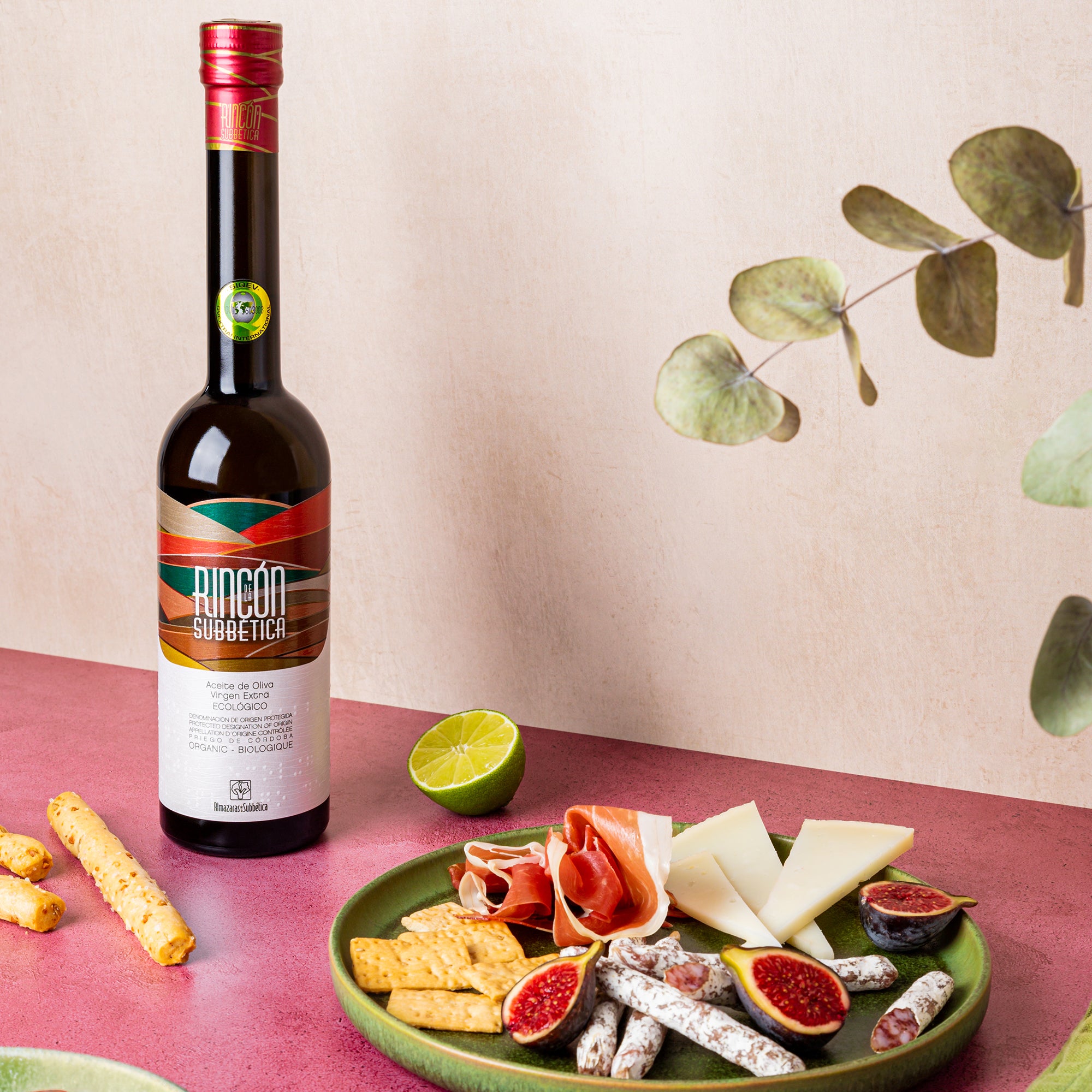 Rincón de la Subbética bottle beside cheese, cured meats, crackers, figs, and lime.