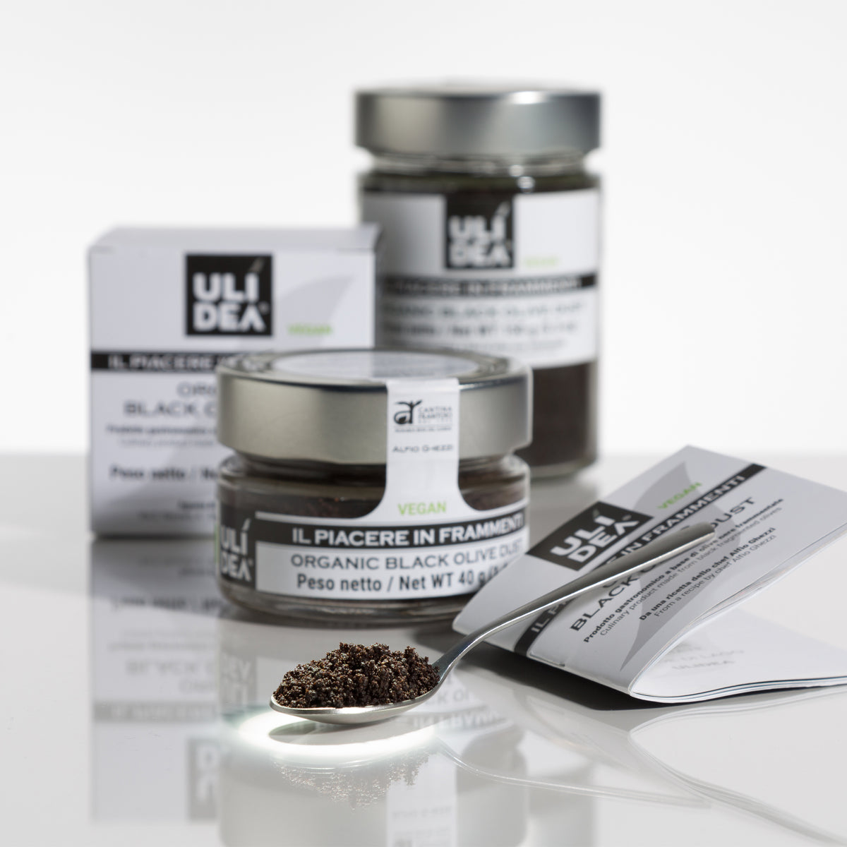 Spoonful of ULIDEA Organic Black Olive Dust with 40g and 150g jars behind.