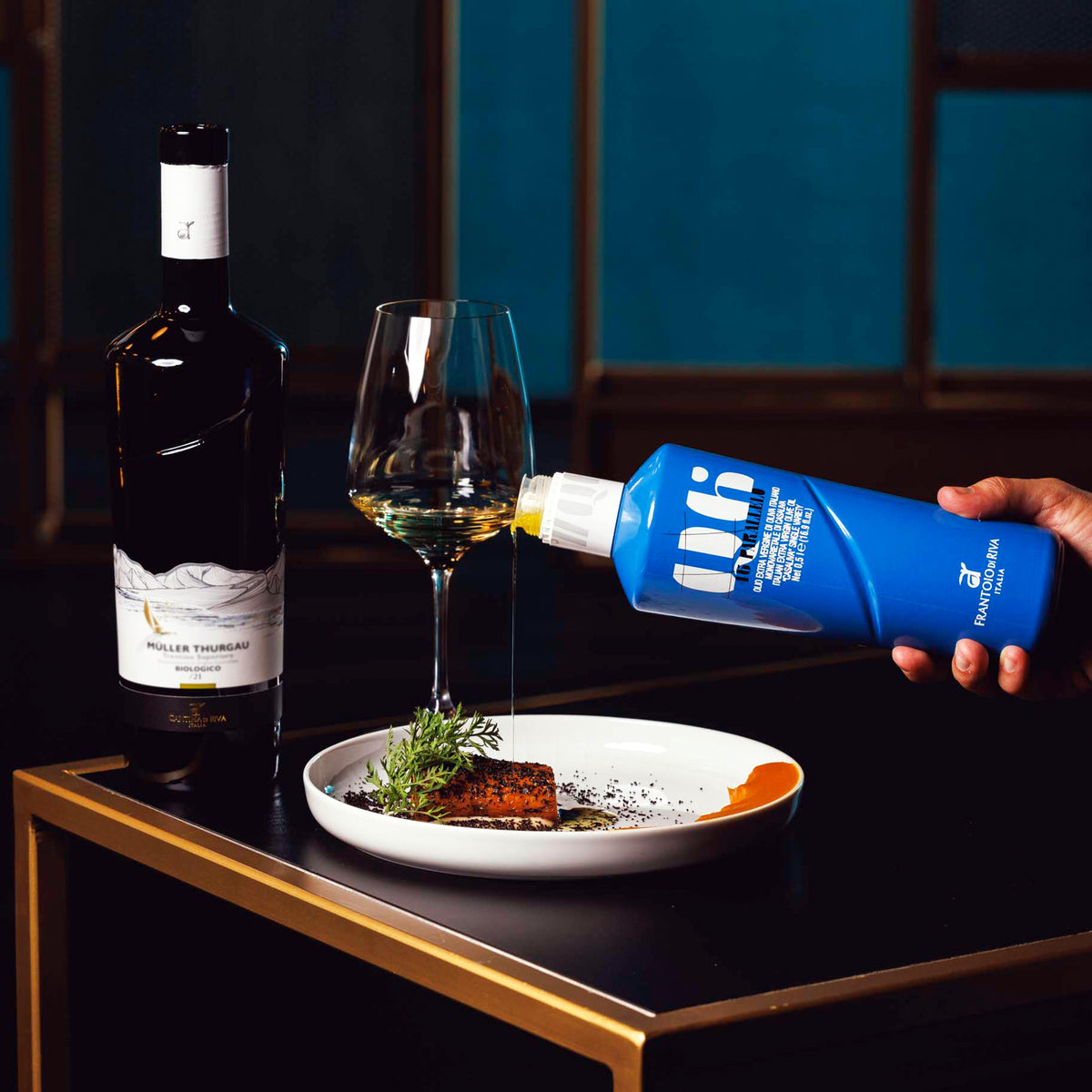 Holding 46° Parallelo Casaliva bottle beside a plated dish, wine glass, and wine bottle.