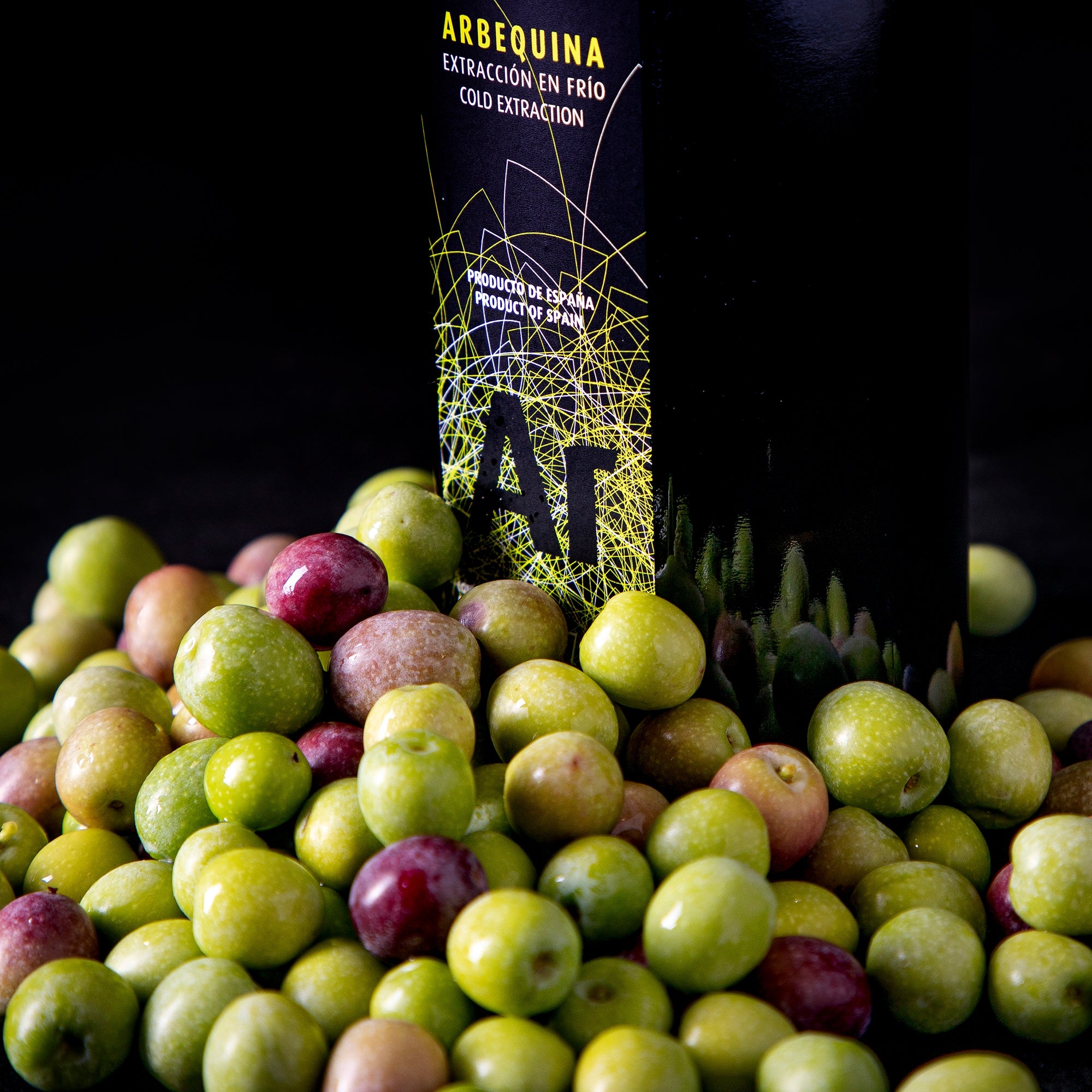 An Oro Bailen Reserva Familiar Arbequina bottle surrounded by fresh olives.
