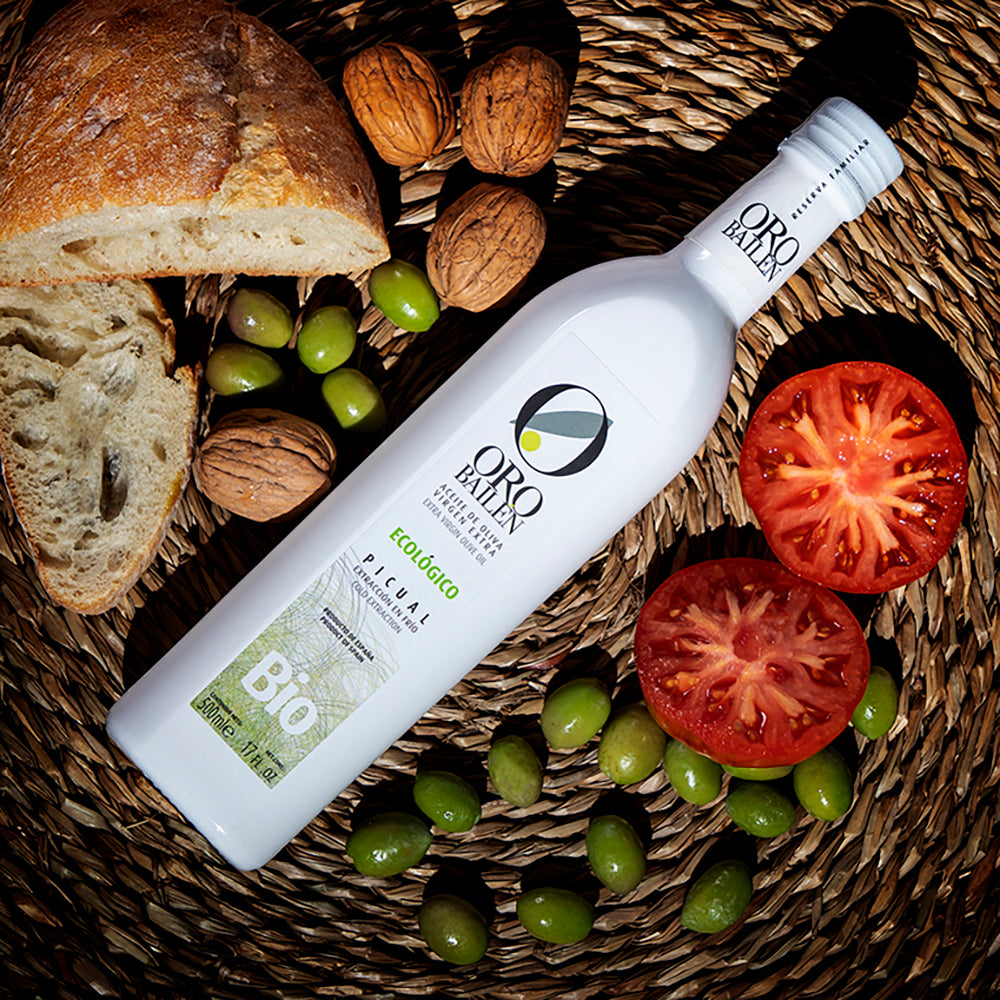Oro Bailen Picual Organic 500 ml bottle with bread, walnuts, green olives, and halved tomatoes.