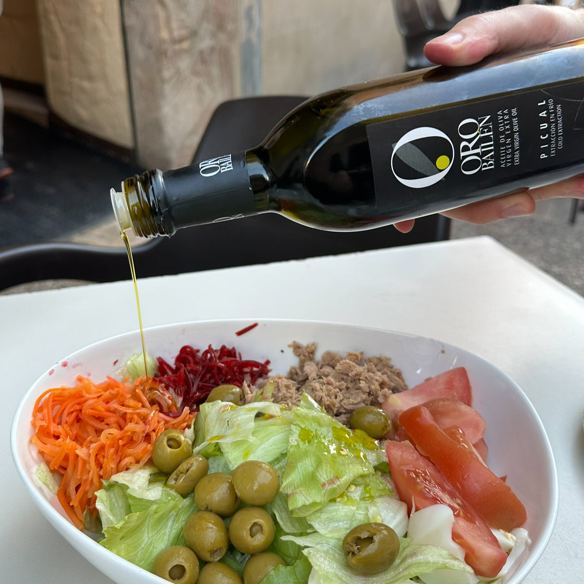 Oro Bailen Picual extra virgin olive oil drizzled over a fresh Mediterranean salad with tuna, olives, and vegetables.