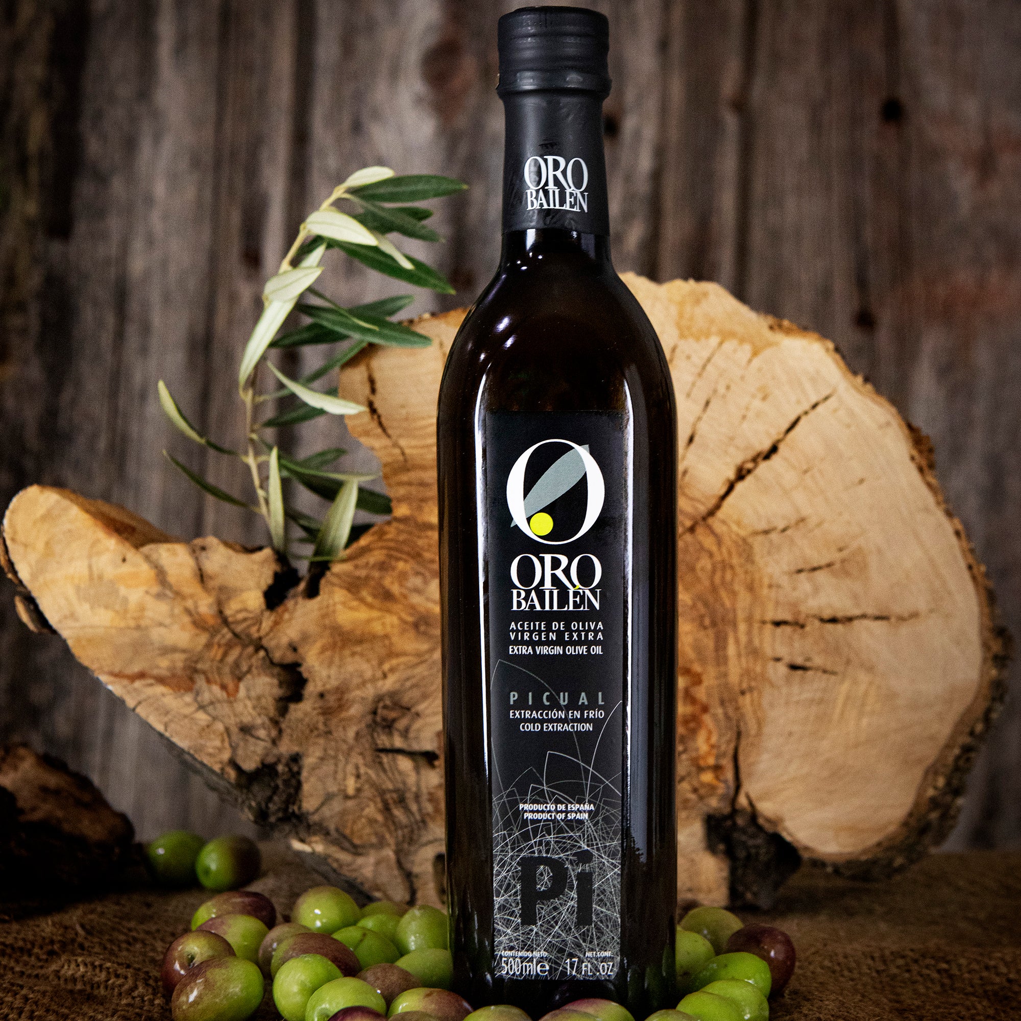 Oro Bailen Reserva Familiar Picual 500ml bottle, fresh olives, and cut logs.