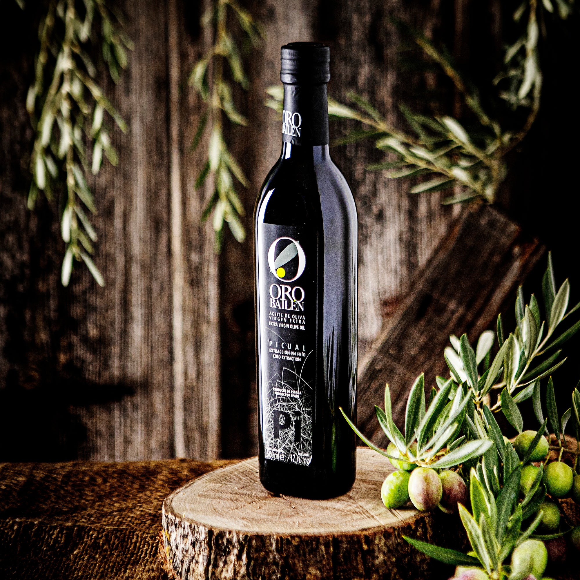 Oro Bailen Reserva Familiar Picual bottle beside olive branches and fresh olives.