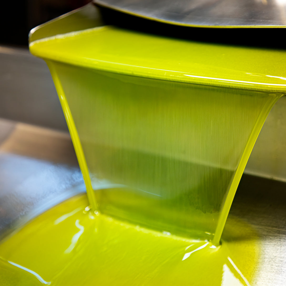Vivid green Picual olive oil flowing from milling equipment during production.