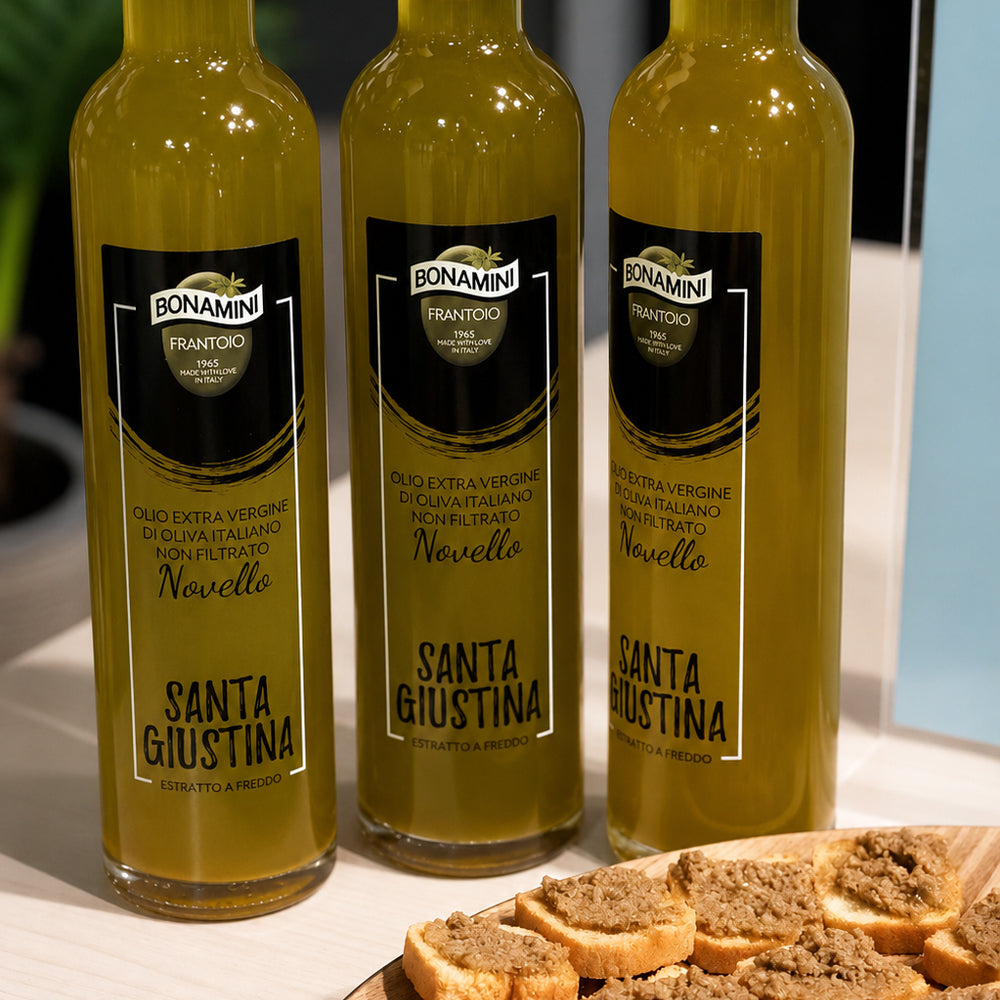 Three Bonamini Santa Giustina Novello 500 ml bottles beside sliced bread topped with olive spread.