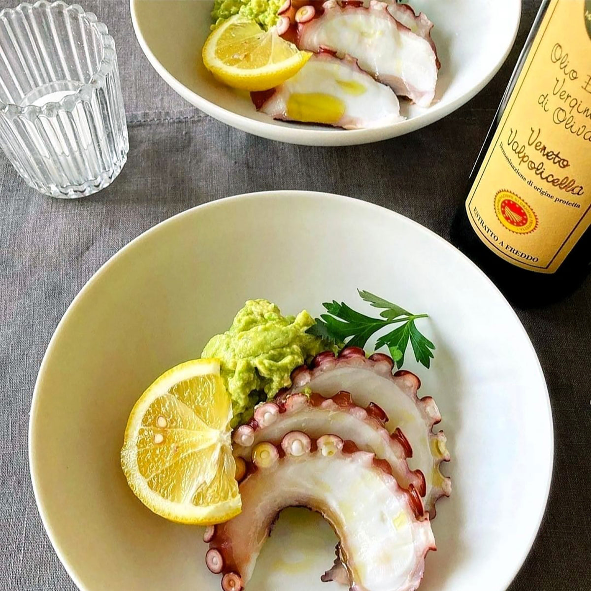 Sliced octopus with lemon and green purée beside a bottle of Frantoio Bonamini DOP Veneto Valpolicella olive oil.