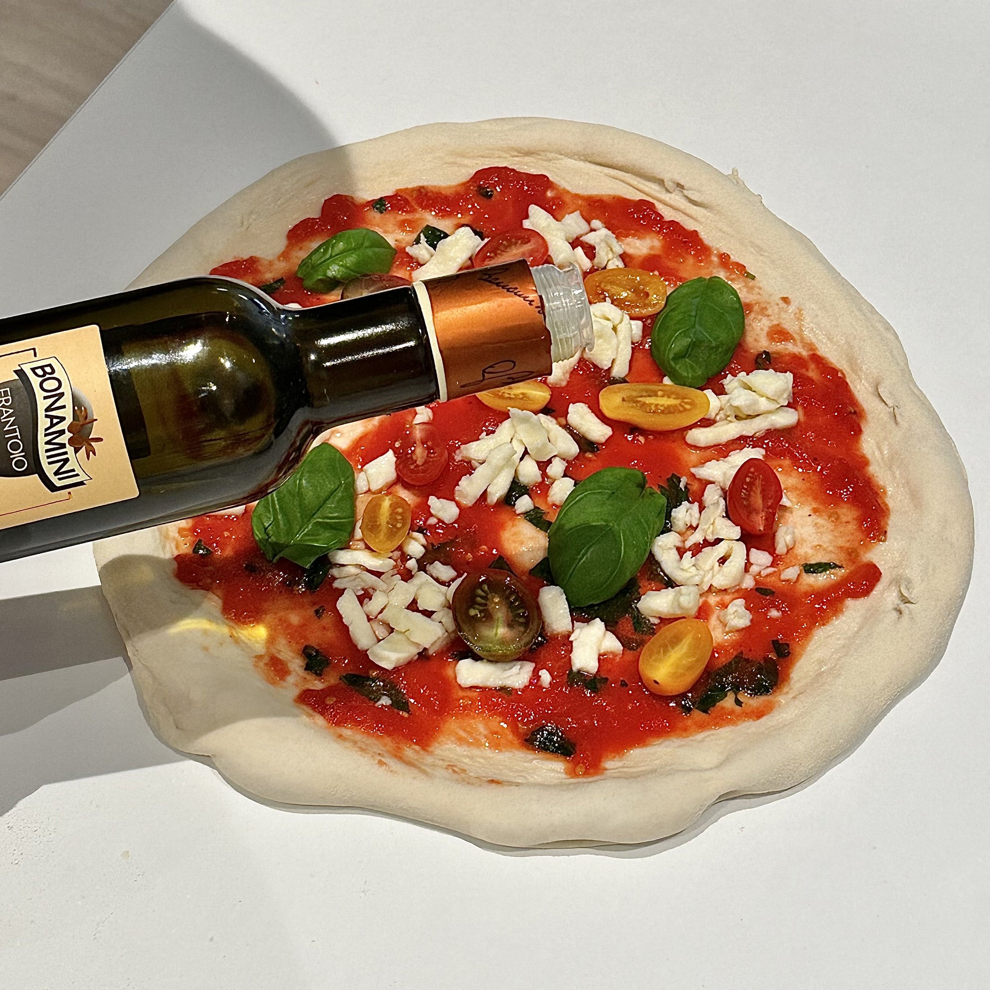 Frantoio Bonamini olive oil being drizzled over an uncooked pizza.