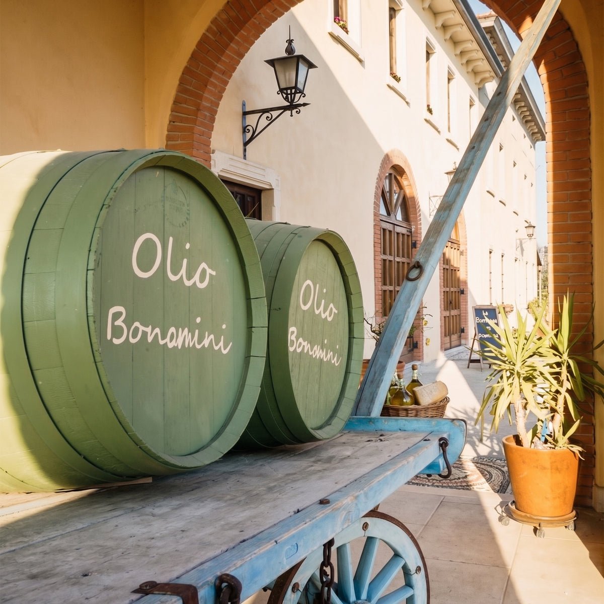 Two green Frantoio Bonamini vinegar barrels on a vintage blue wooden cart.