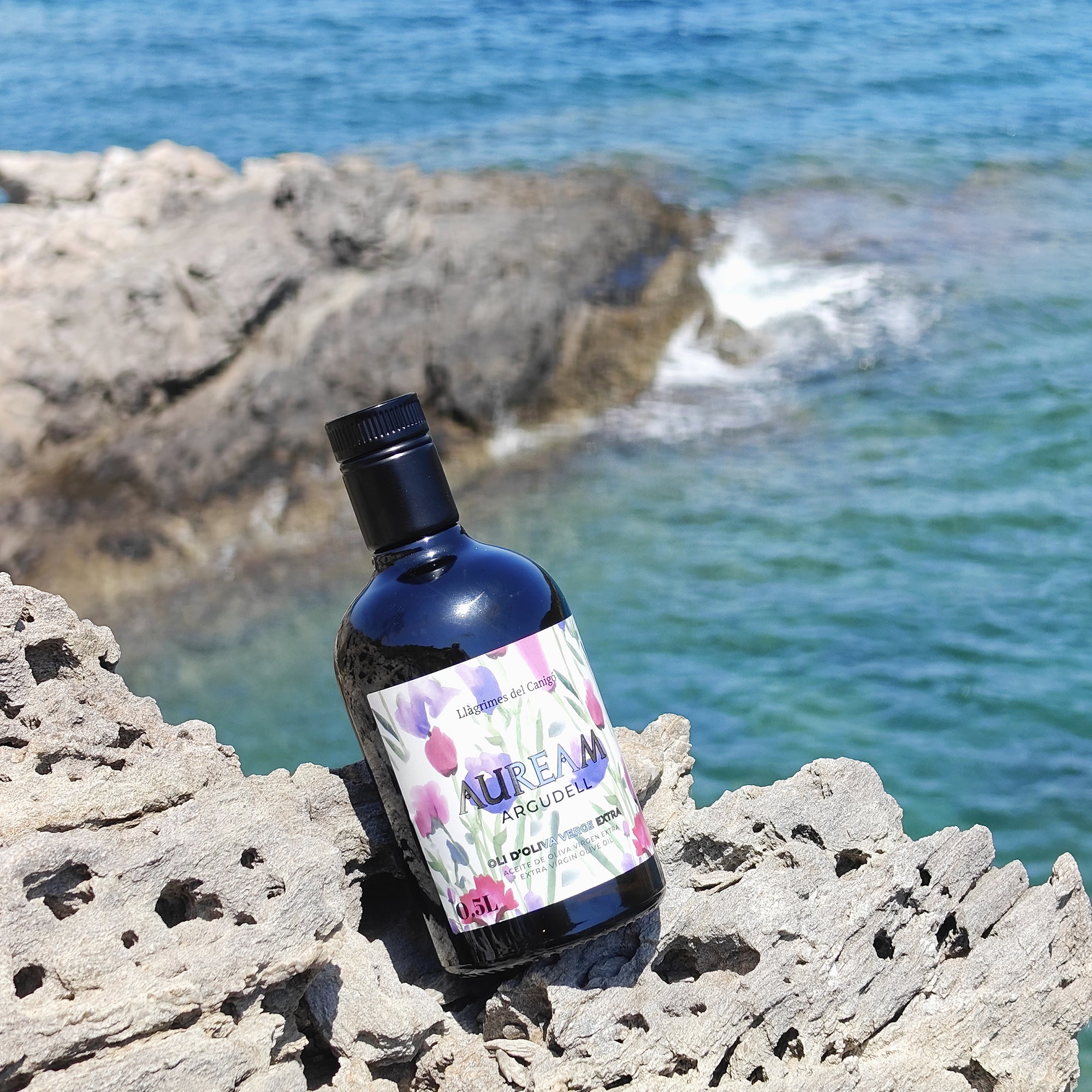 Auream Argudell 500 ml extra virgin olive oil bottle on rugged seaside rocks.