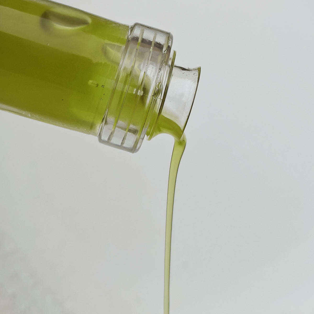 Vibrant green Oli del Raig Novello pouring from the 500 ml glass bottle.