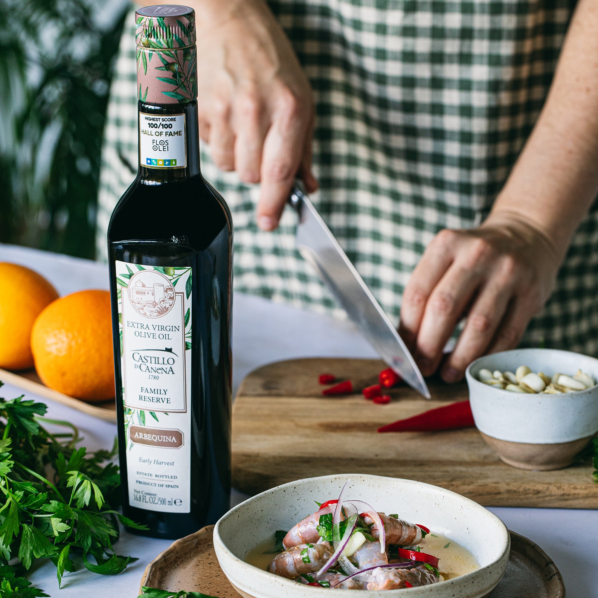 Castillo de Canena Family Reserve Arbequina 500 ml bottle beside a cook preparing peppers and a seafood dish.
