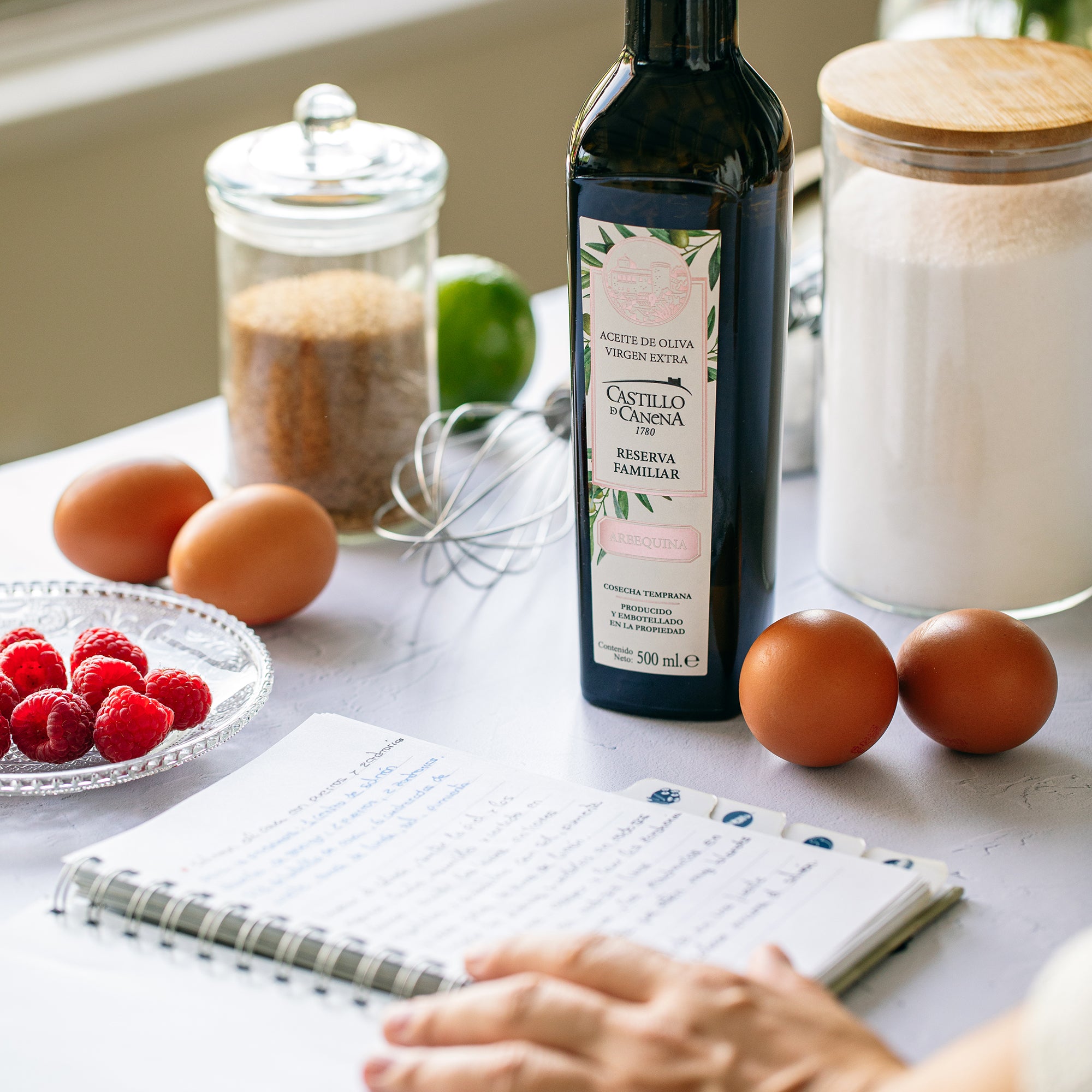 Castillo de Canena Family Reserve Arbequina 500 ml bottle next to eggs, raspberries, flour, and baking ingredients.