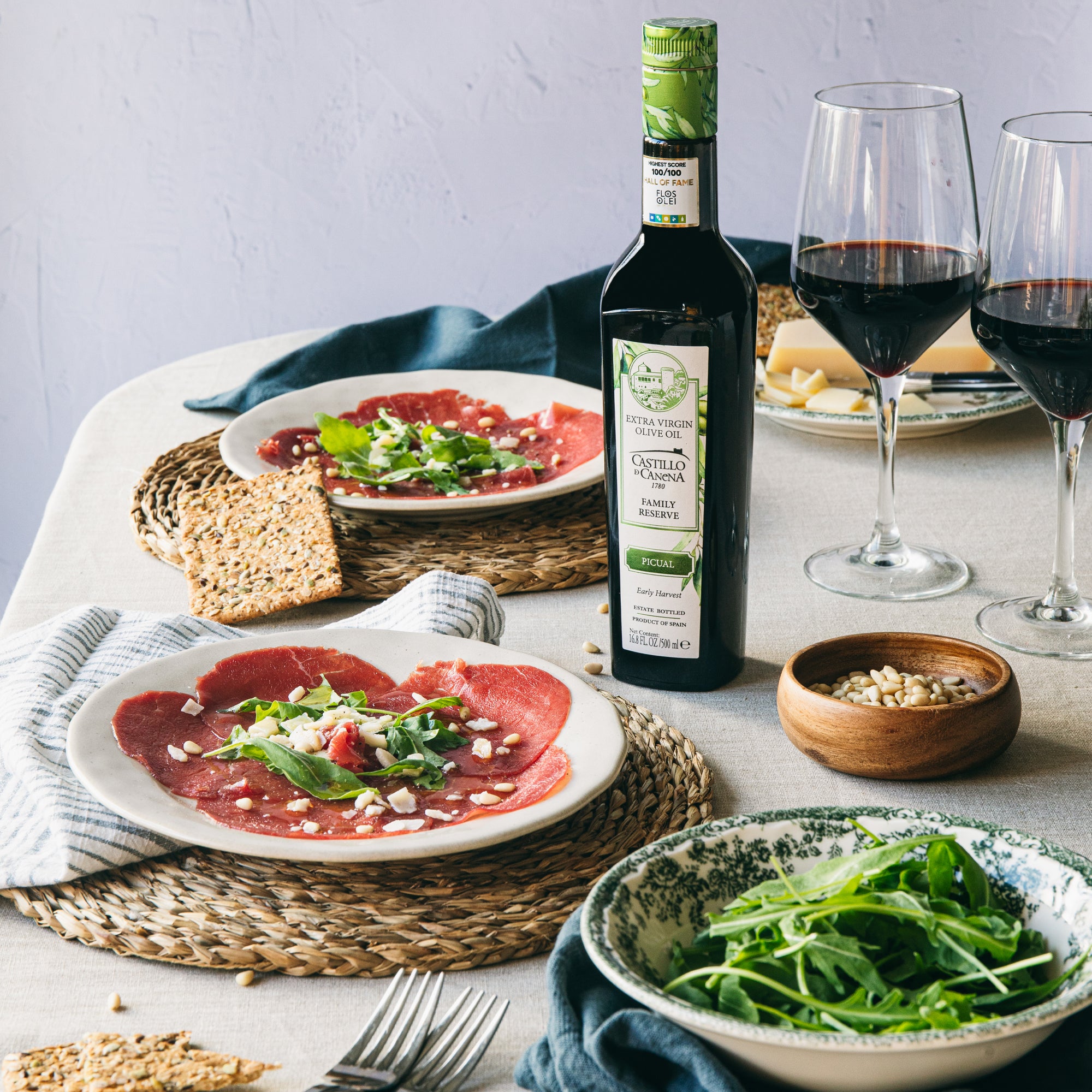 Castillo de Canena Family Reserve Picual bottle with beef carpaccio, arugula, cheese, pine nuts, and red wine.