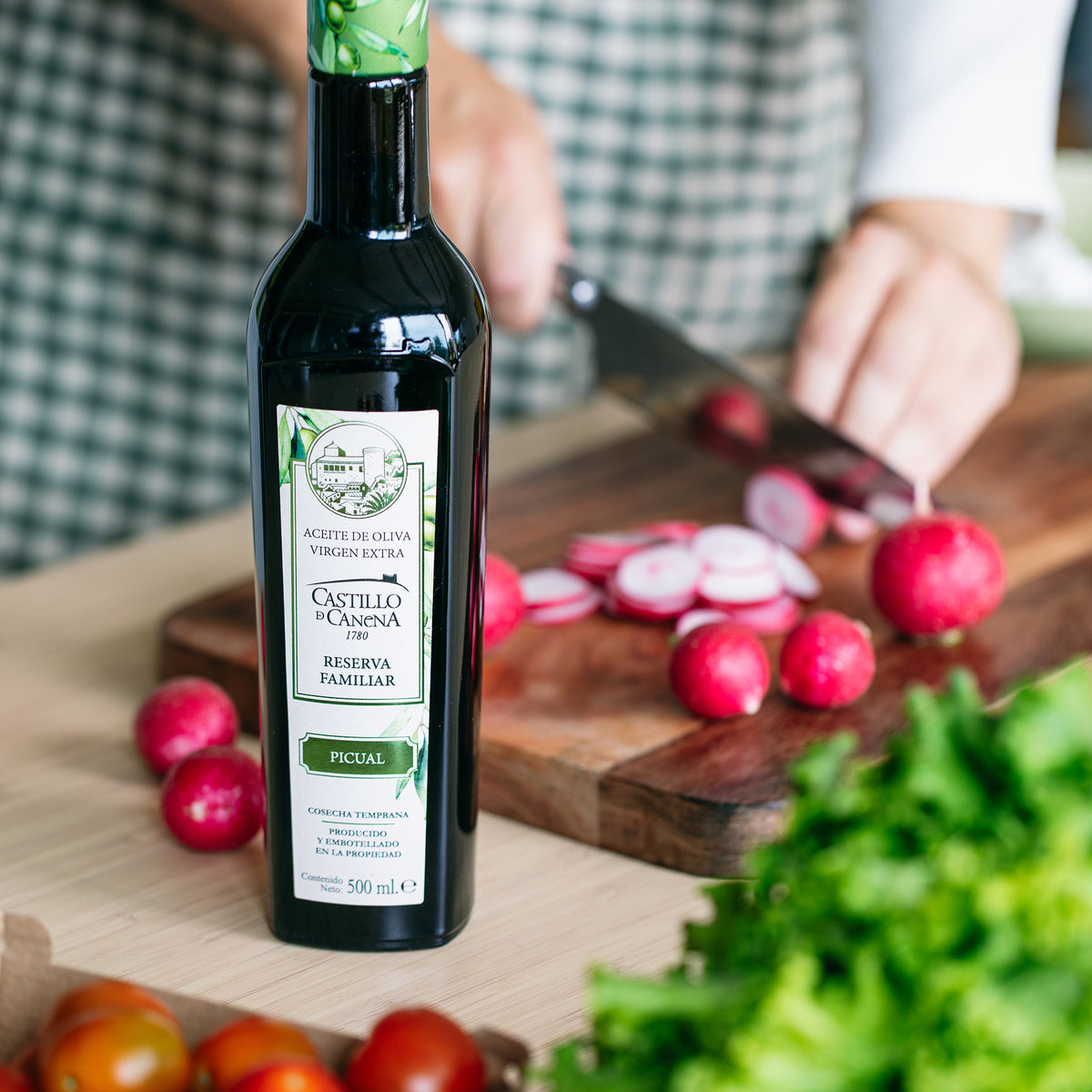 Castillo de Canena Family Reserve Picual extra virgin olive oil beside a person slicing red radishes.