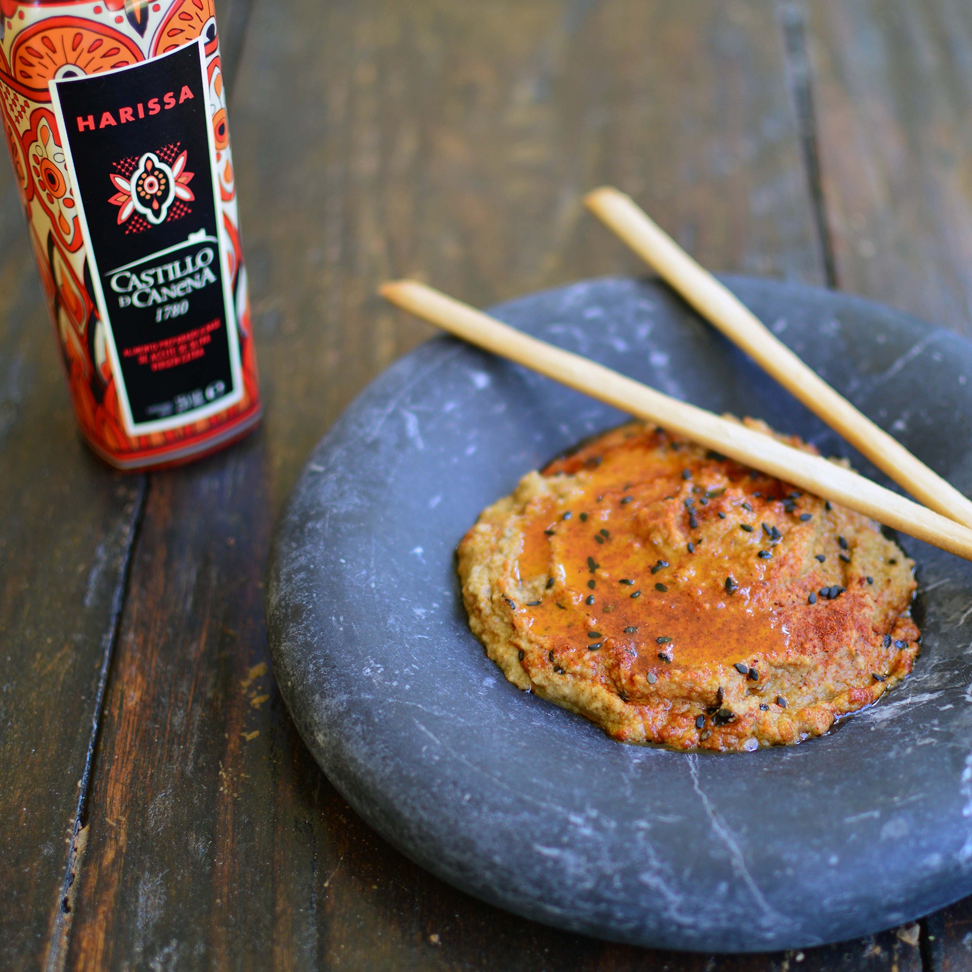 Castillo de Canena Harissa Arbequina bottle beside a seasoned dish served with wooden chopsticks.