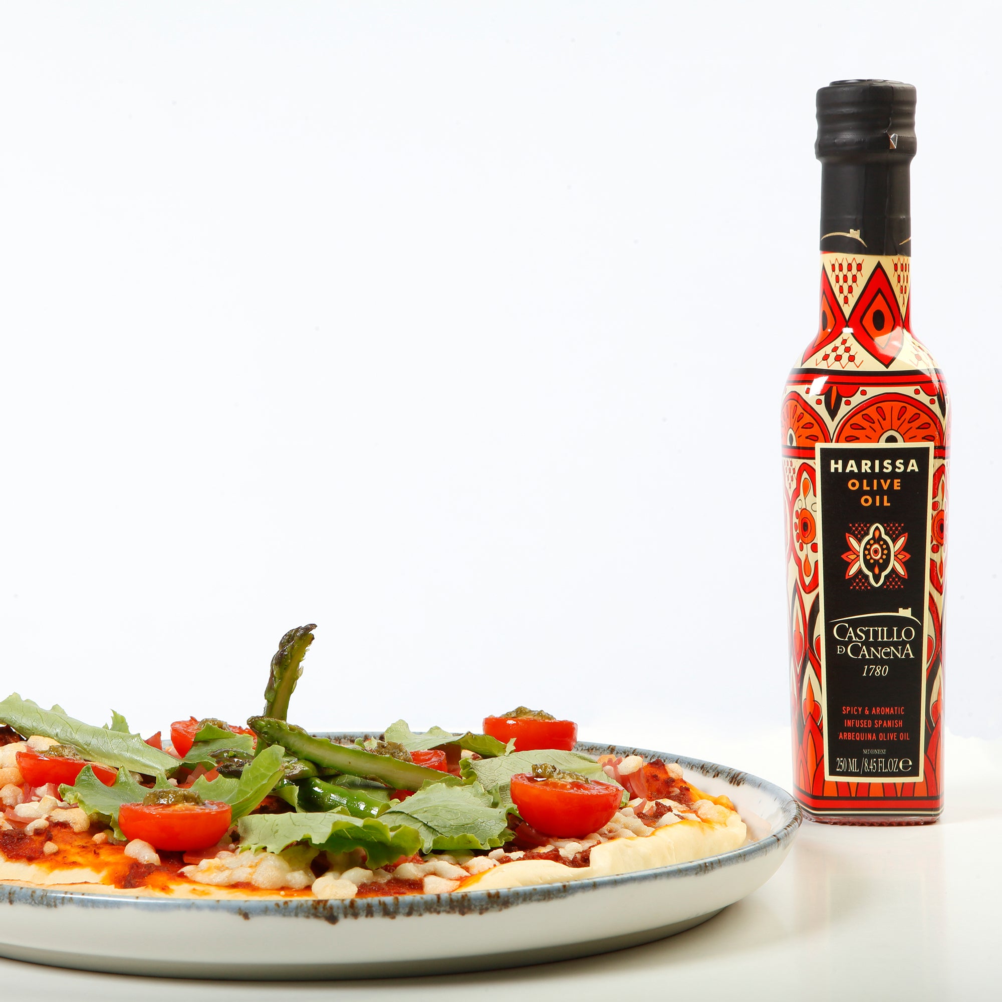 Castillo de Canena Harissa Arbequina beside a vegetable-topped flatbread with asparagus and tomatoes.