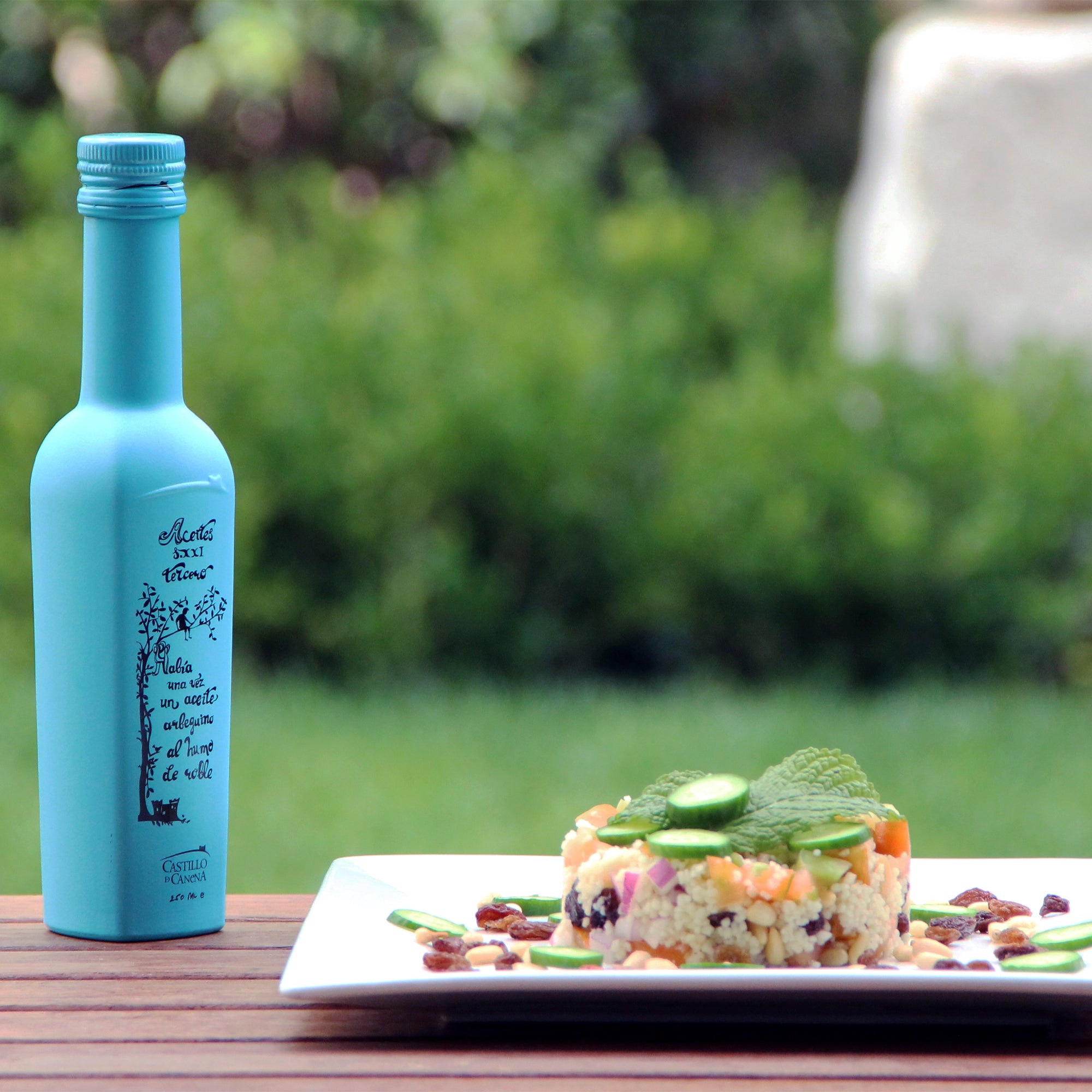 Castillo de Canena Smoked Arbequina bottle beside a cucumber-topped couscous salad.