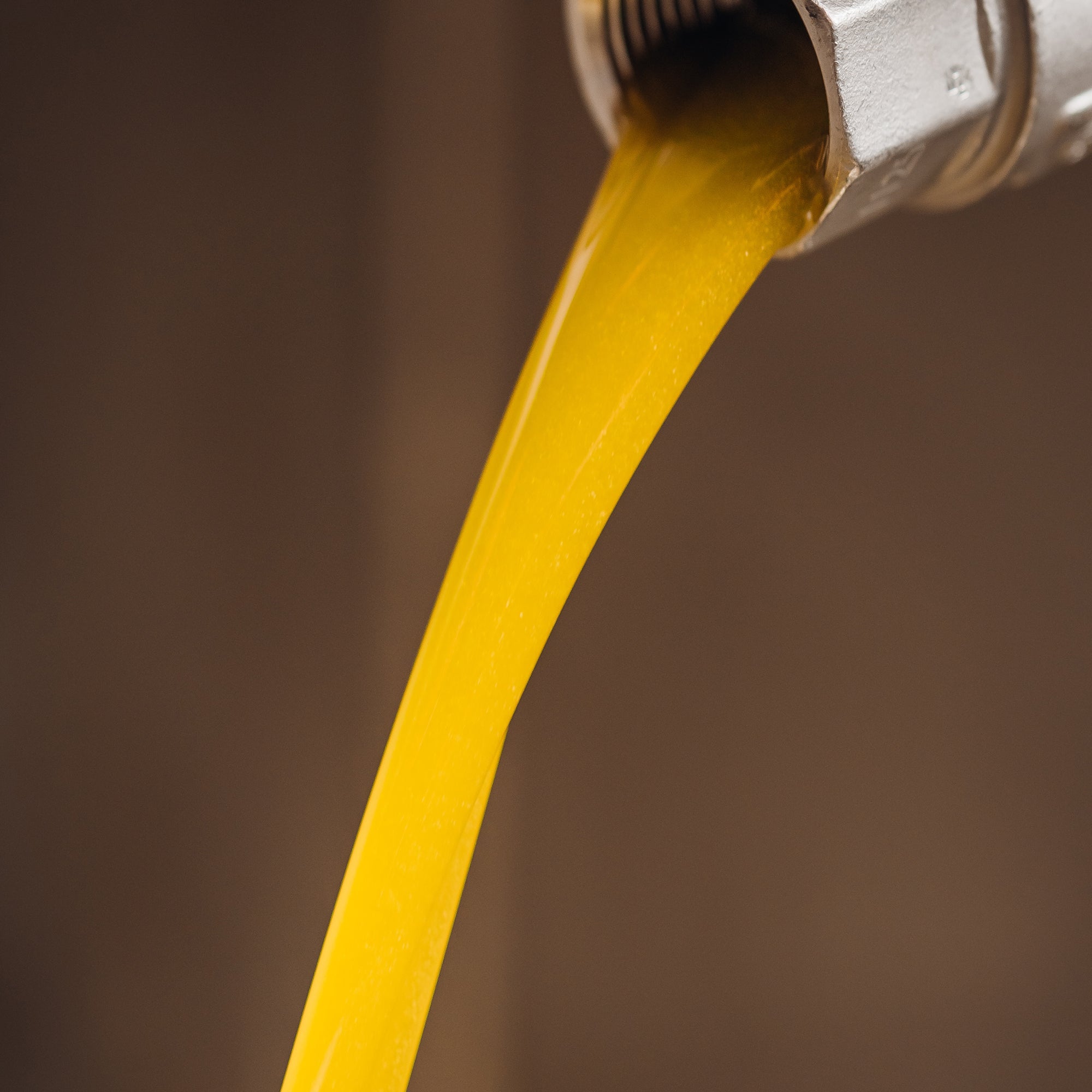 Freshly extracted olive oil flowing from a metal press outlet.