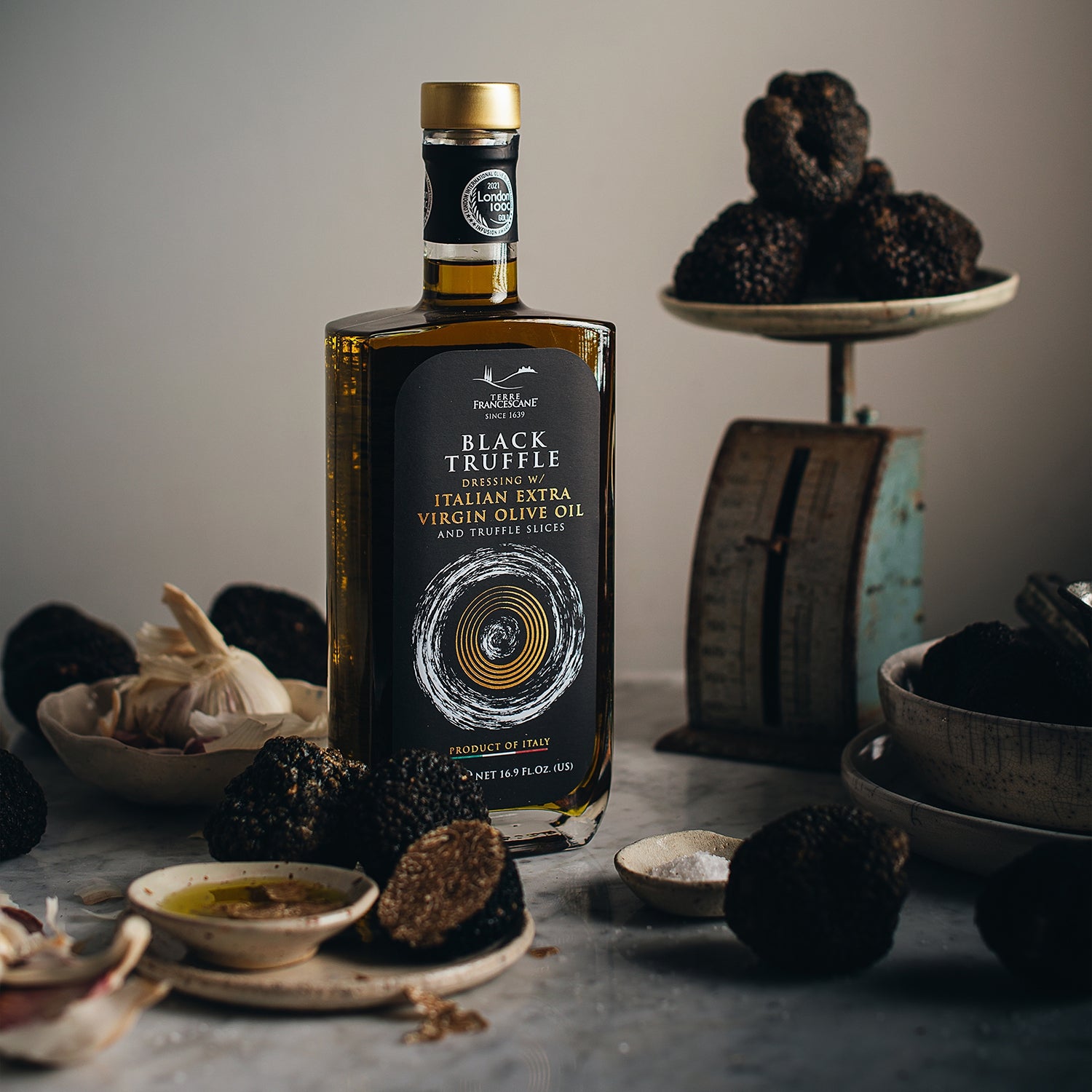 Terre Francescane Black Truffle 500 ml bottle among whole black truffles, garlic, salt, and olive oil.