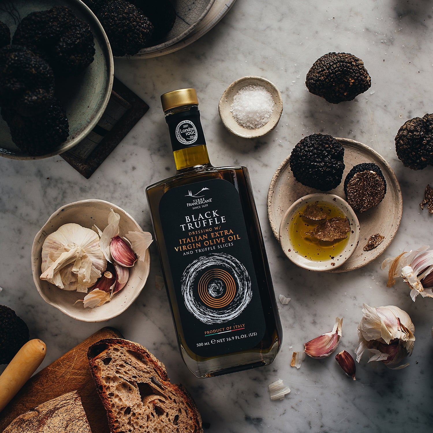 Terre Francescane Black Truffle 500 ml bottle beside black truffles, garlic, bread, salt, and olive oil.