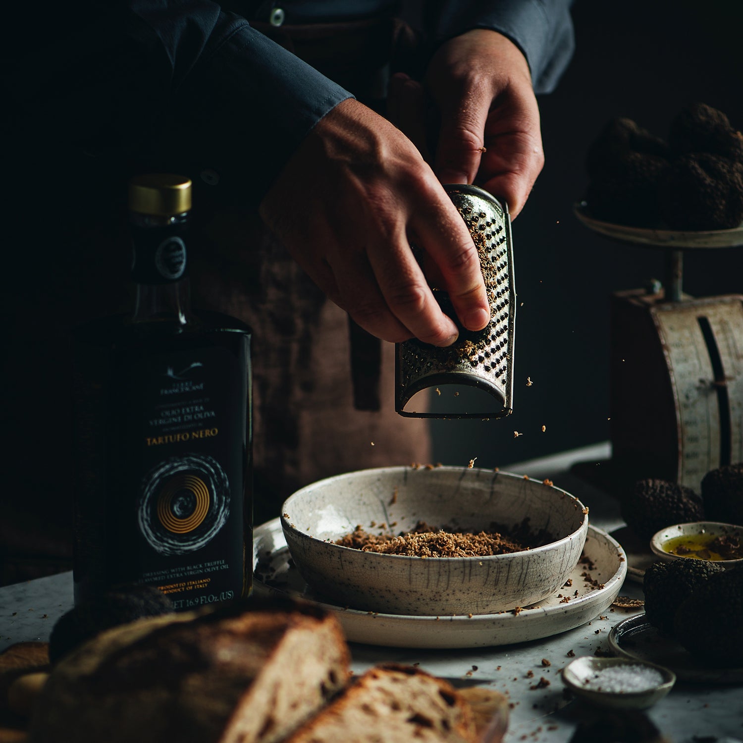 Grating black truffle over a bowl beside Terre Francescane Black Truffle olive oil.
