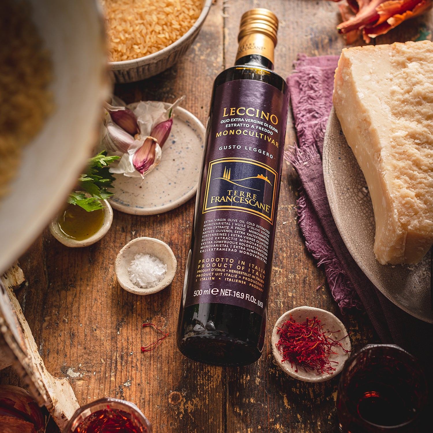 Terre Francescane Leccino 500 ml bottle beside Parmesan, garlic, saffron, and parsley.