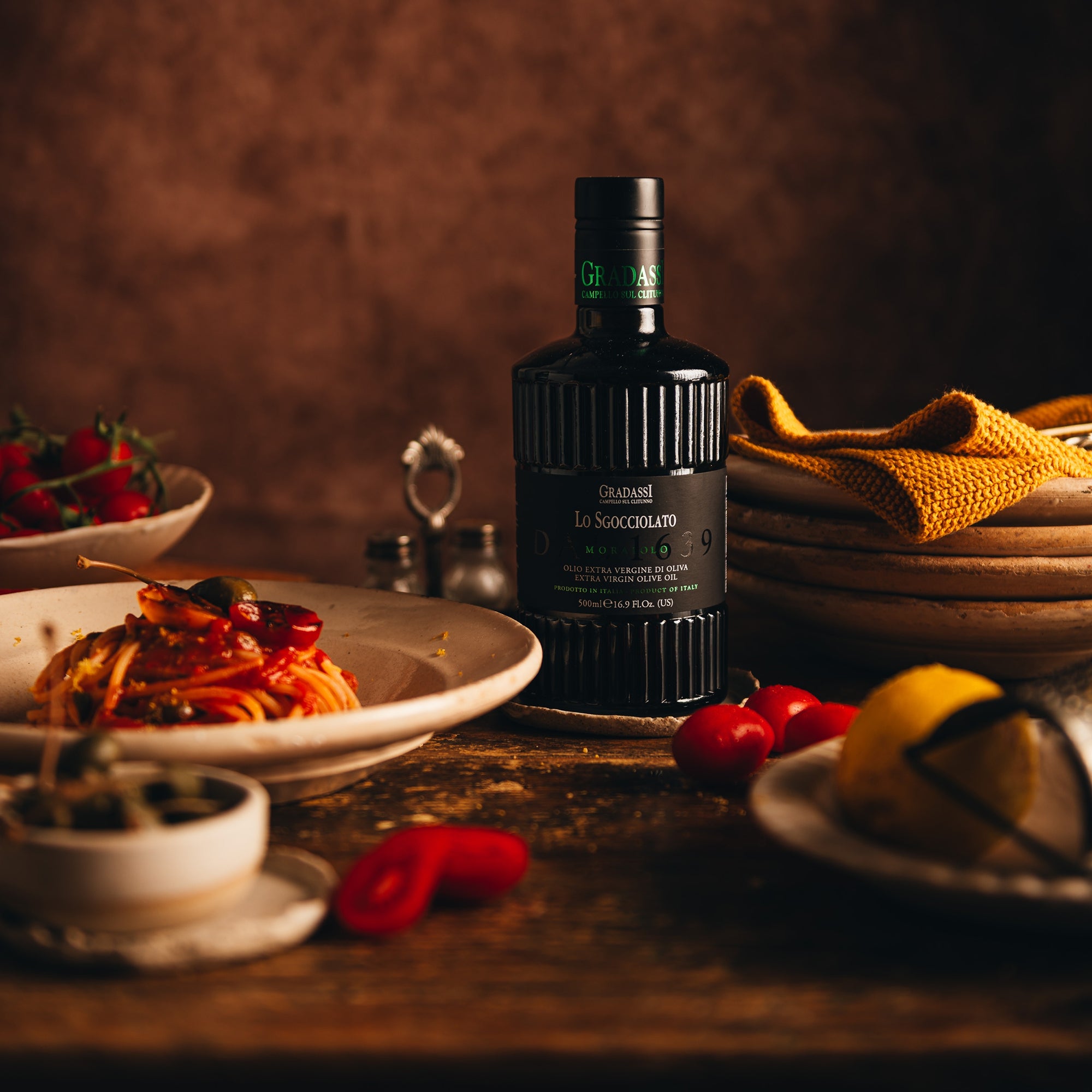 Gradassi Lo Sgocciolato Moraiolo 500 ml bottle beside tomato pasta, fresh tomatoes, and lemons.