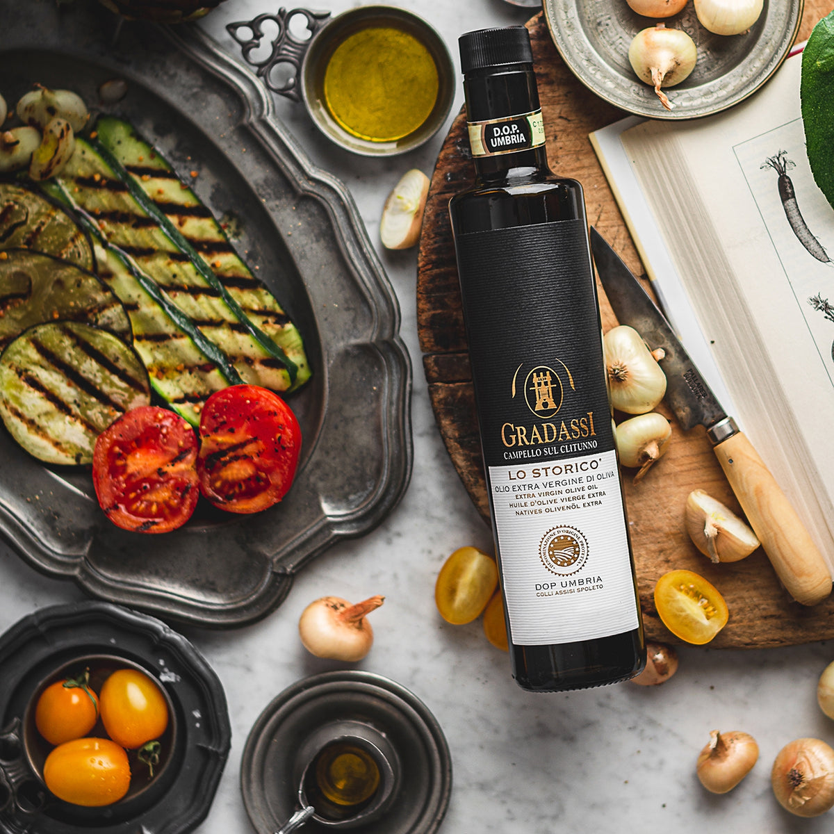 750 ml bottle of Gradassi Lo Storico extra virgin olive oil beside grilled vegetables, tomatoes, and onions.