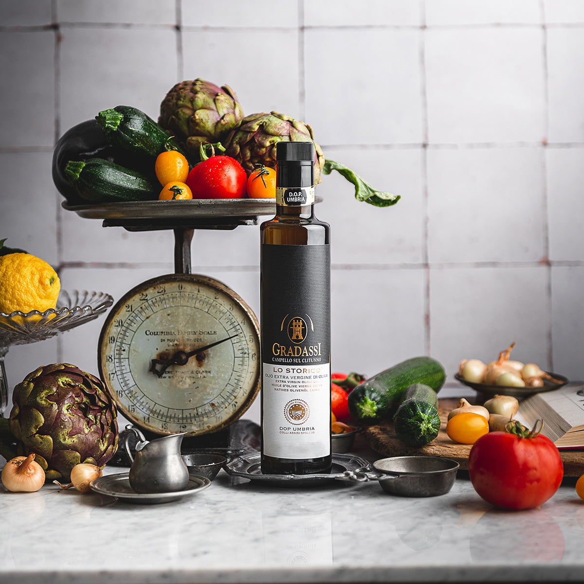 Gradassi Lo Storico 750 ml bottle, with fresh artichokes, zucchini, tomatoes, onions, and a vintage kitchen scale.
