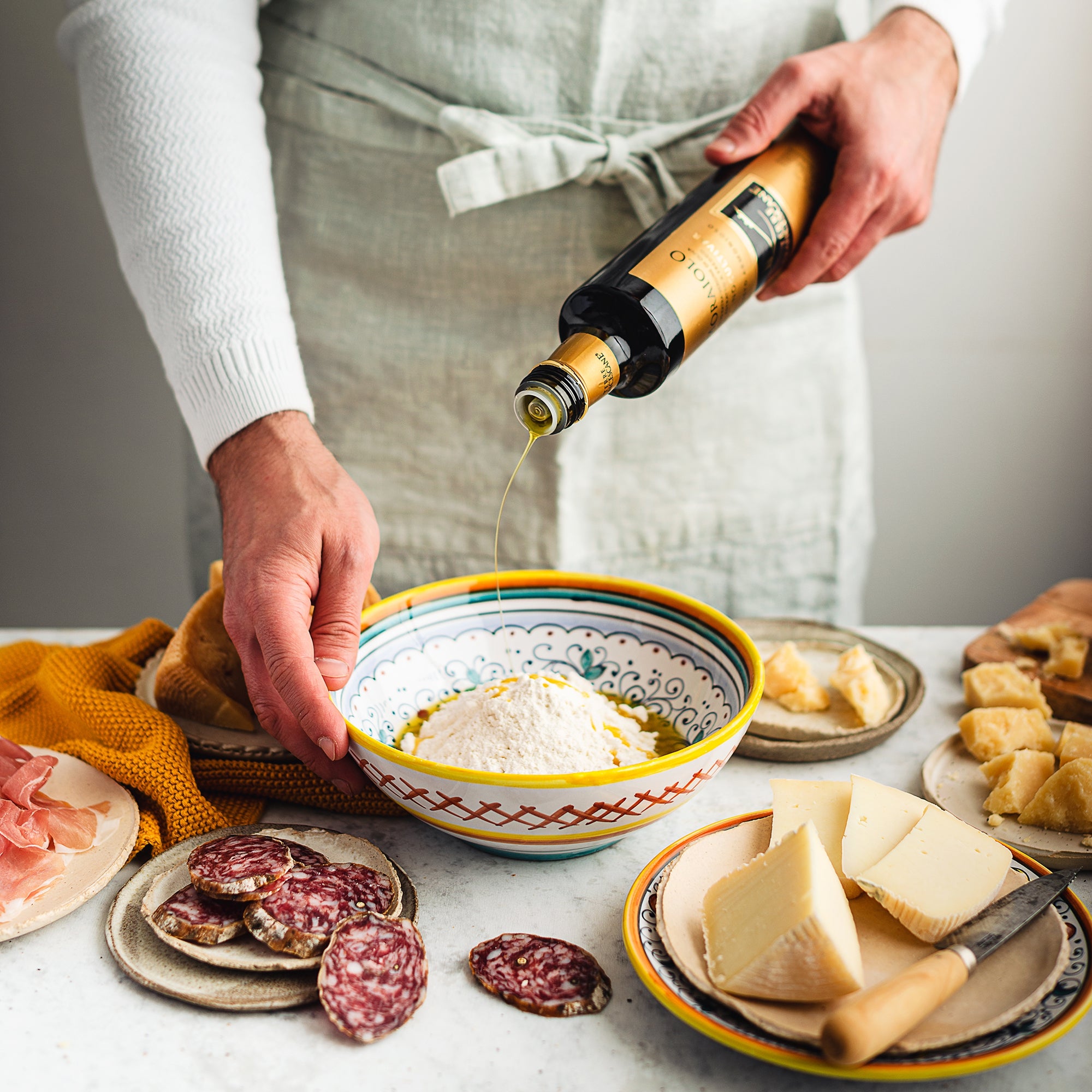 Terre Francescane Moraiolo 500 ml olive oil being poured over ricotta, surrounded by cheeses and cured meats.