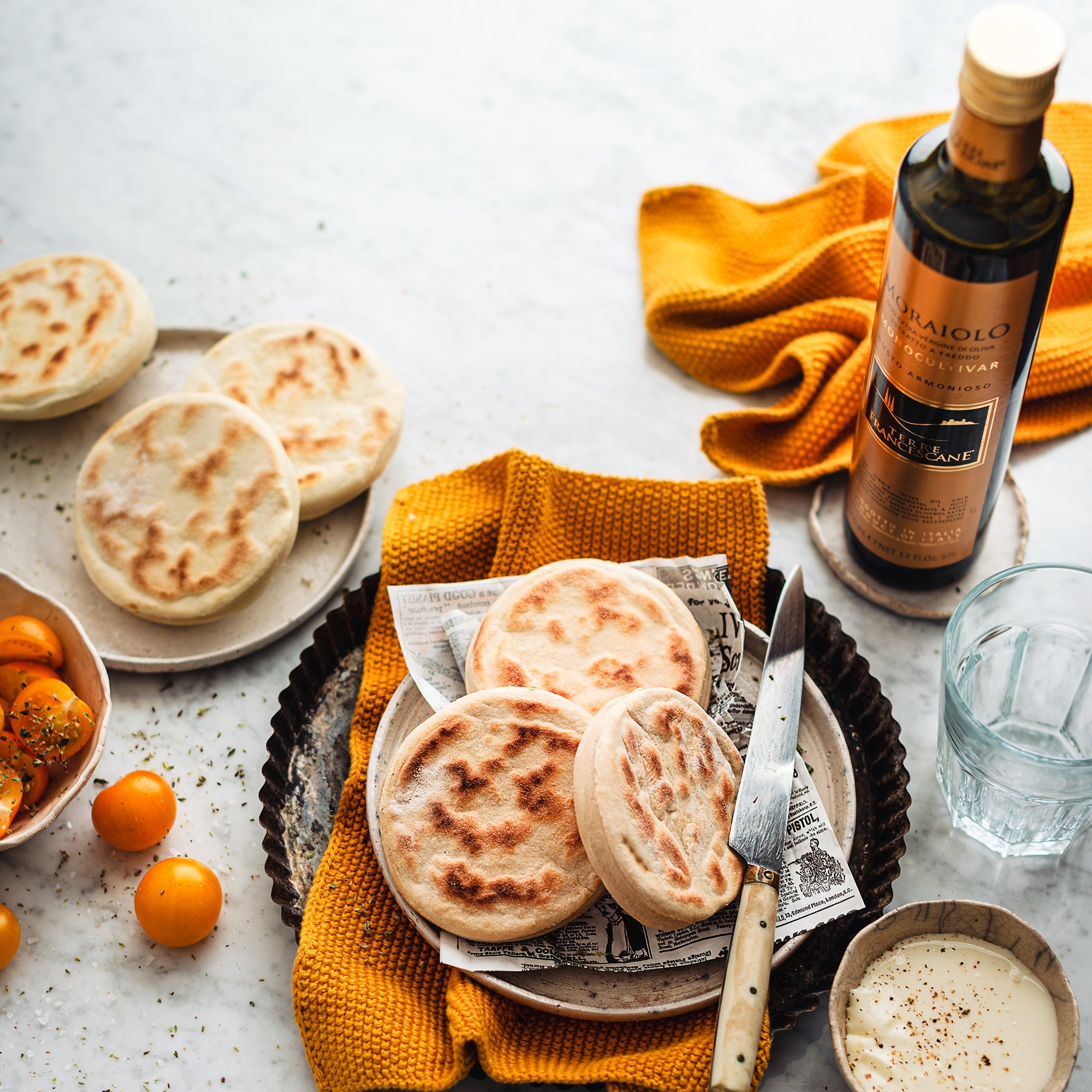 Terre Francescane Moraiolo olive oil bottle beside flatbreads, and tomatoes.