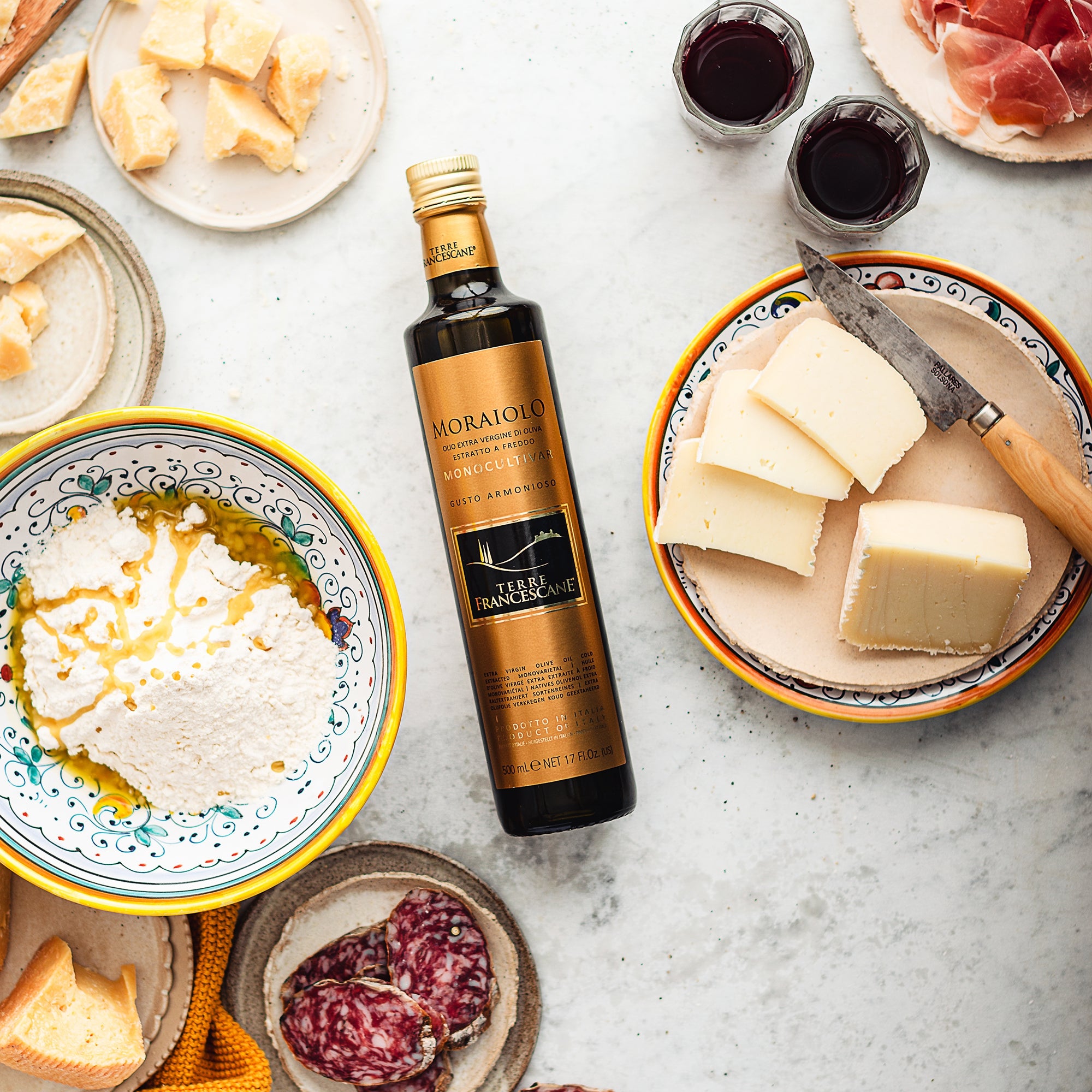 500 ml Terre Francescane Moraiolo bottle surrounded by cheeses, cured meats, ricotta, and glasses of red wine.