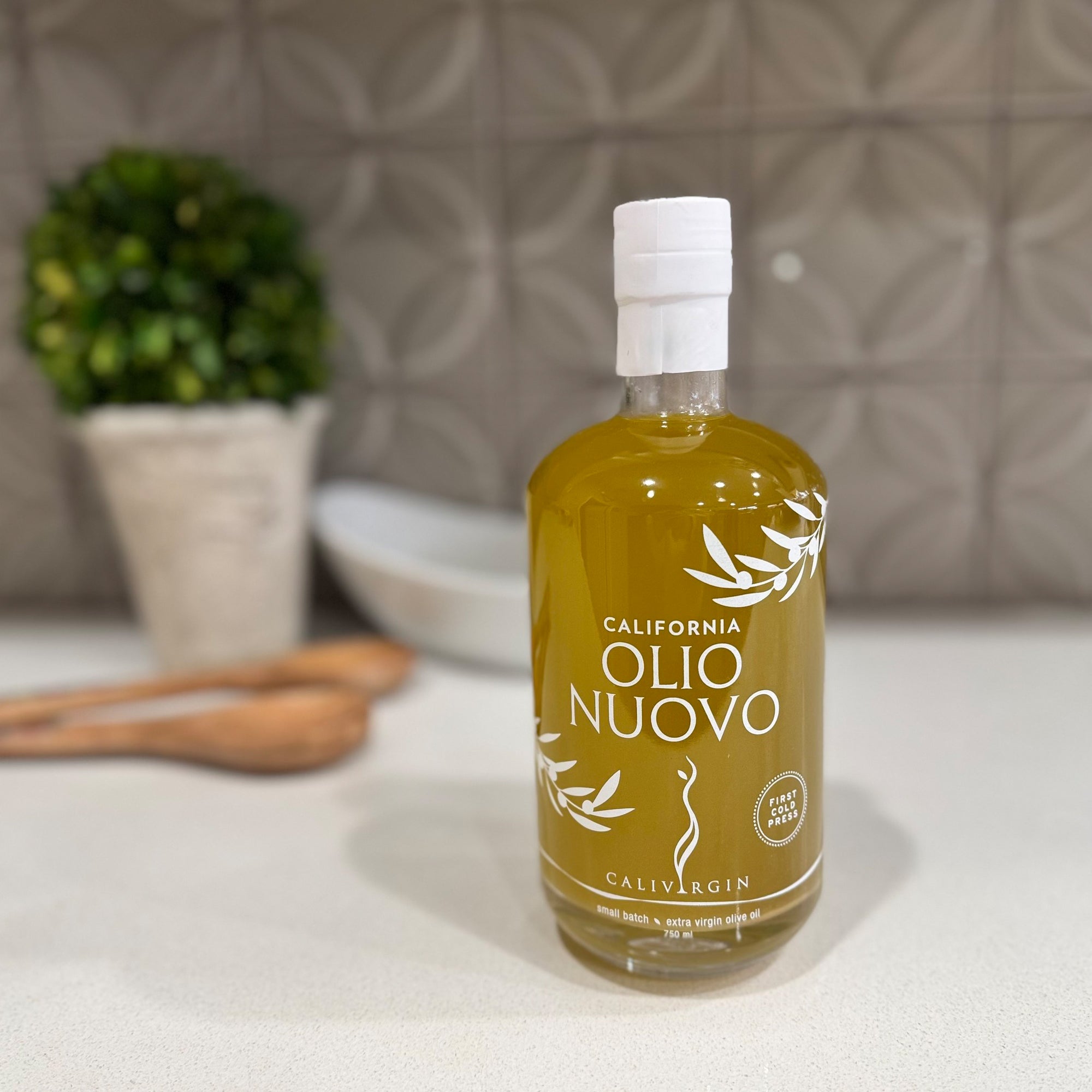 Calivirgin Olio Nuovo bottle on a kitchen counter beside wooden utensils.
