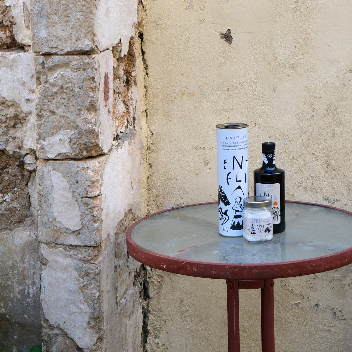 Entelia 1L extra virgin olive oil can, Entelia Novello, and Entelia Pyramid Sea Salt on an outdoor table.