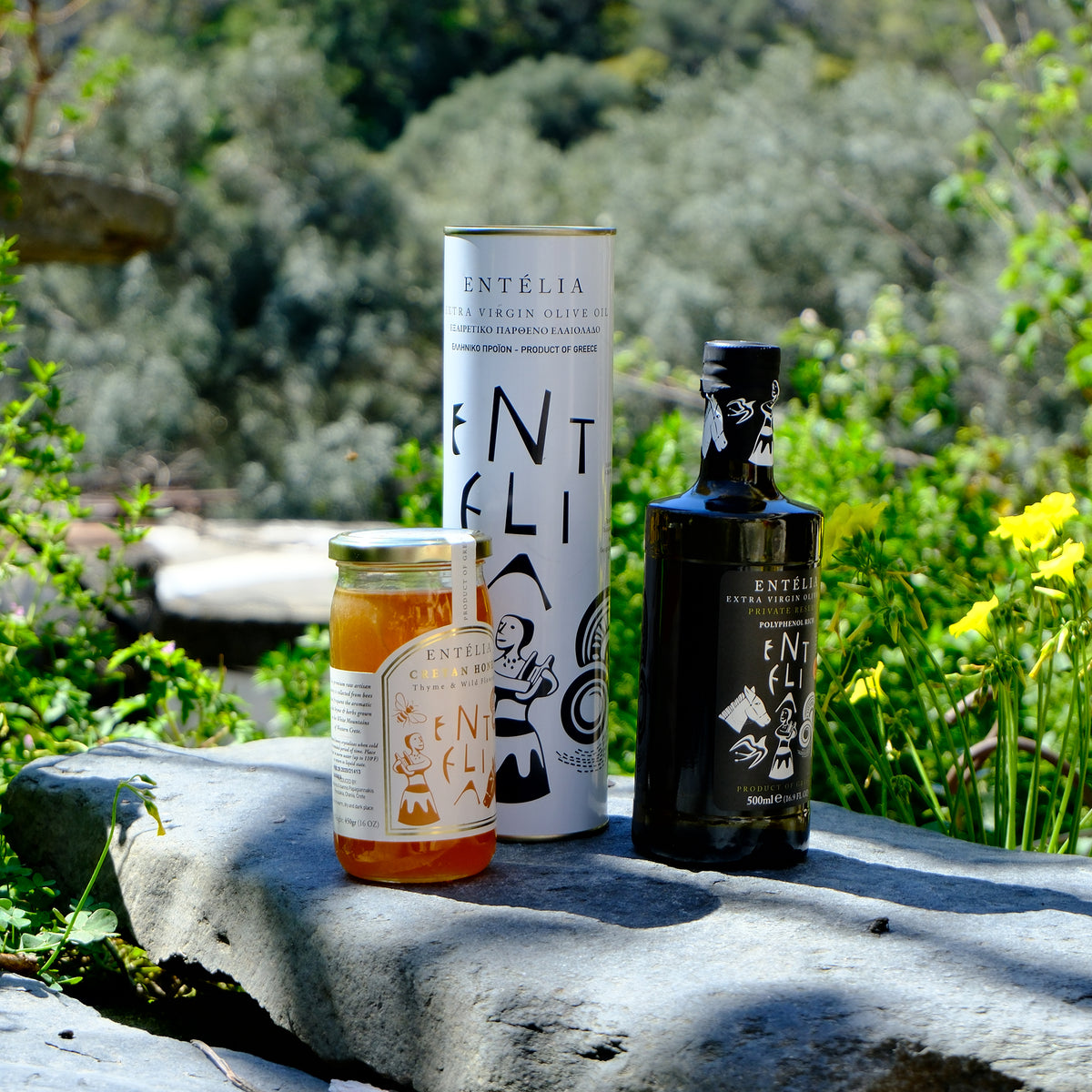 Entelia 1L olive oil can, Entelia Private Reserve, and Entelia Cretan honey, among lush greenery.