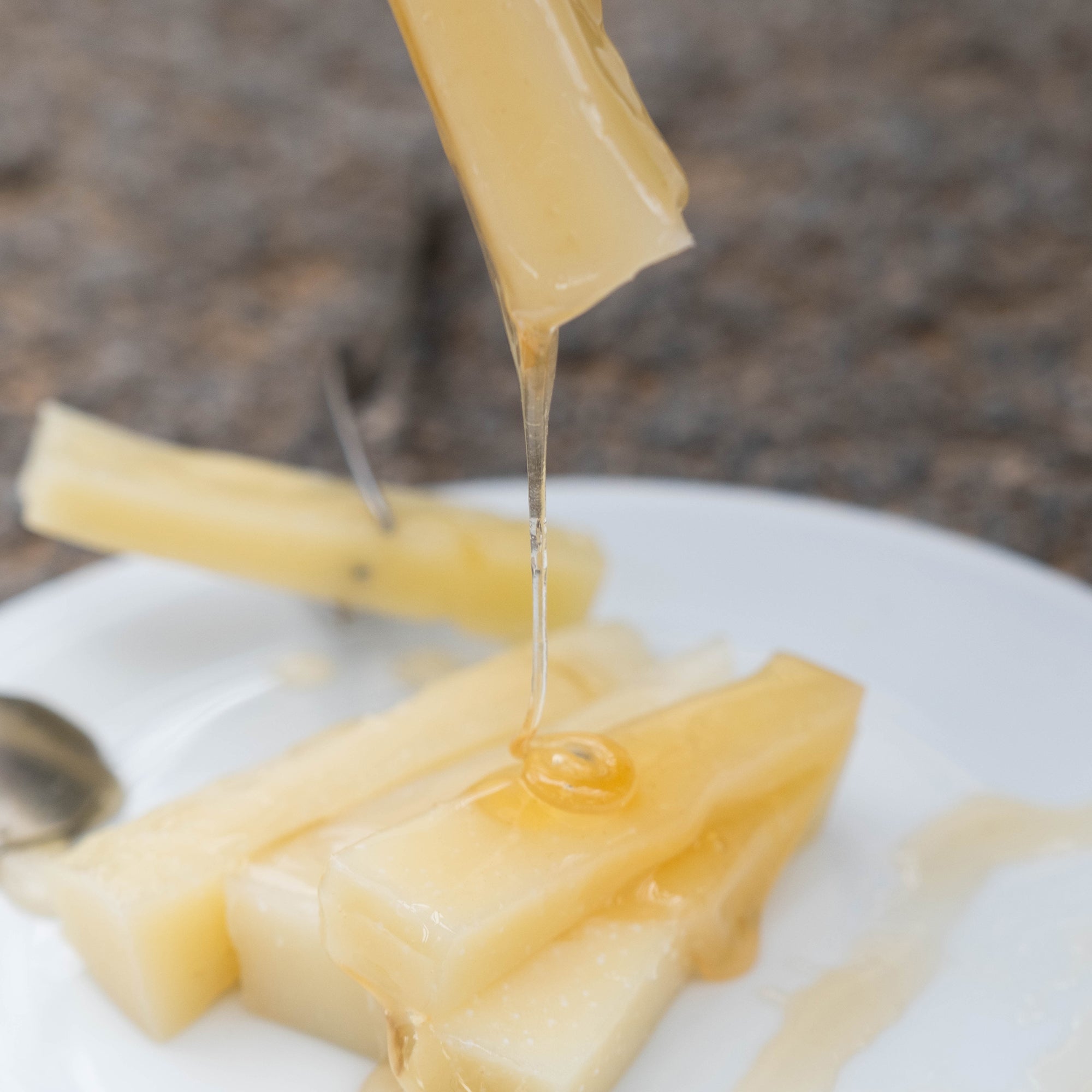 Entelia Cretan Honey drizzling from a piece of cheese onto sliced cheese.