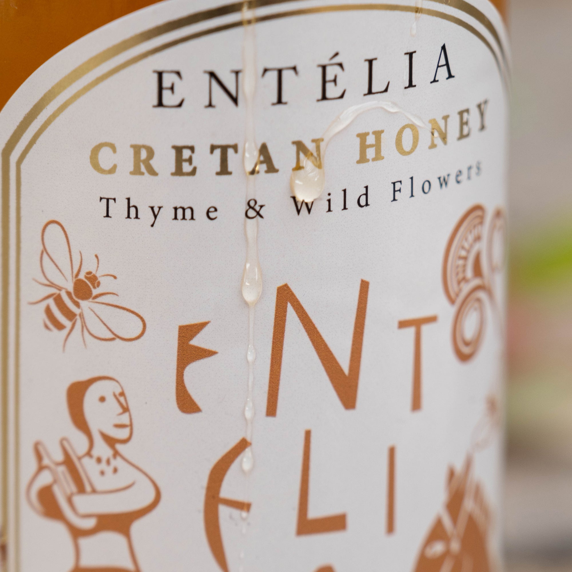 Honey droplets running over the label of an Entelia Thyme & Wild Flowers Cretan Honey jar.