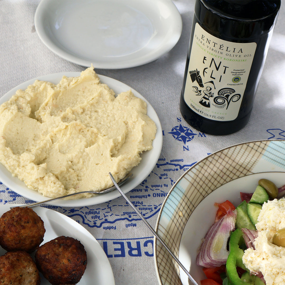 Entelia extra virgin olive oil bottle beside Greek salad, and meatballs.
