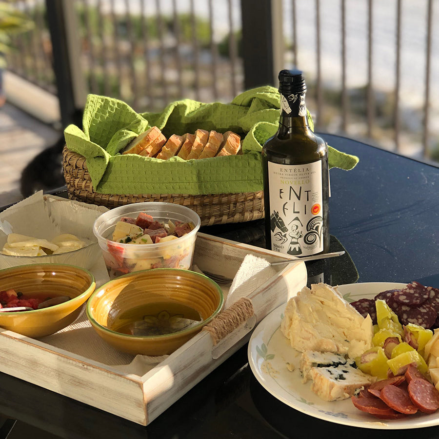 Entelia Novello 500ml olive oil beside bread, cheeses, olives, and cured meats.