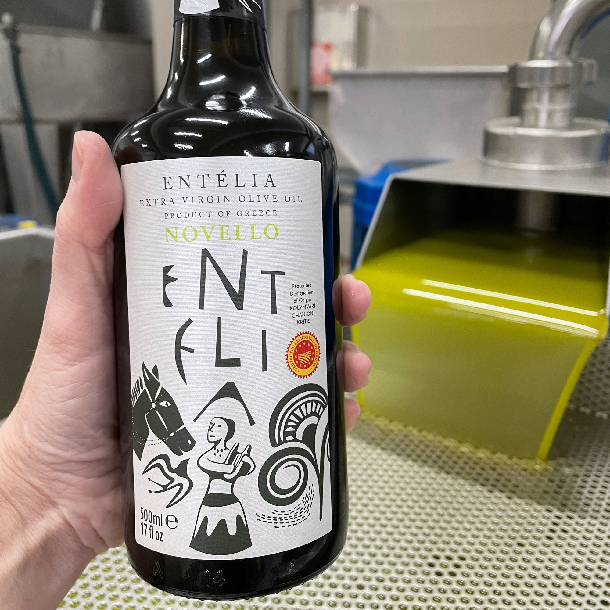 Holding Entelia Novello 500ml bottle beside freshly extracted green olive oil.