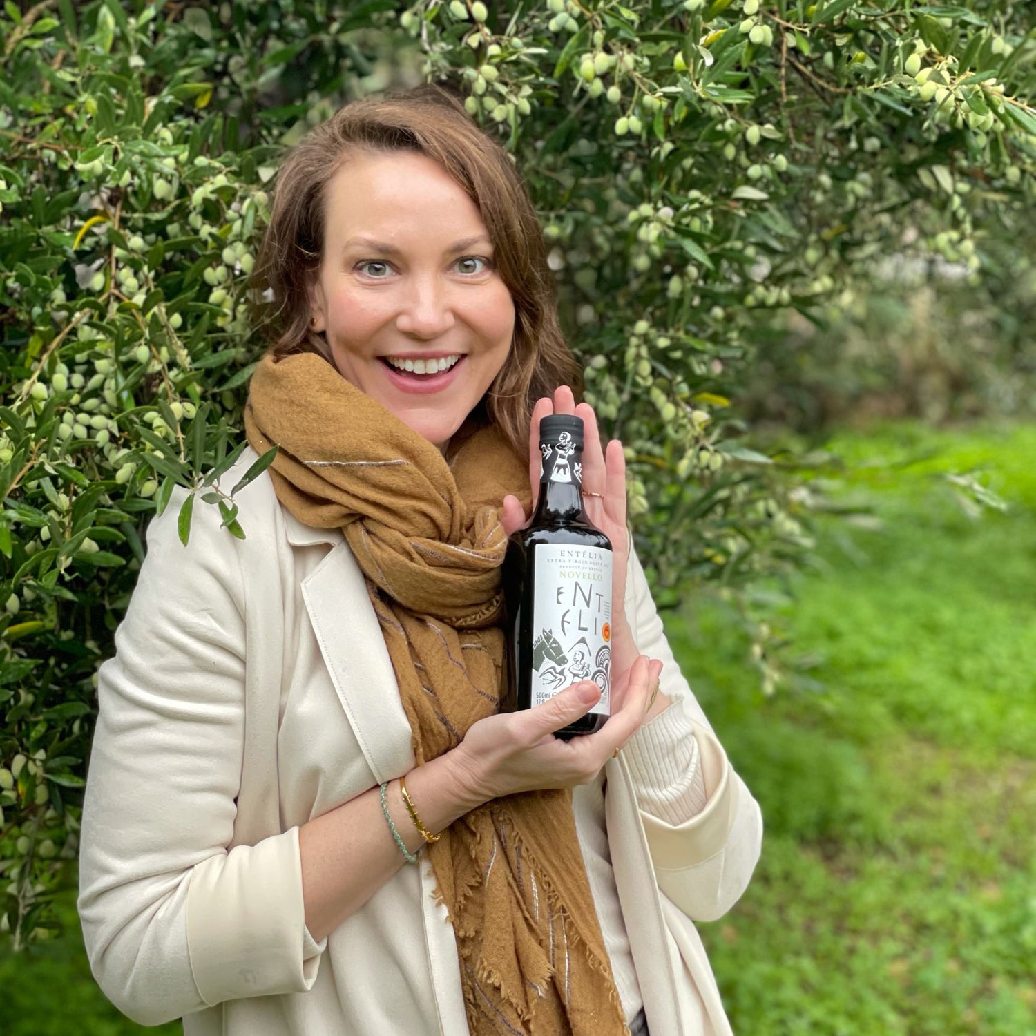 Joanne Lacina holding Entelia Novello 500ml olive oil bottle in an olive grove.