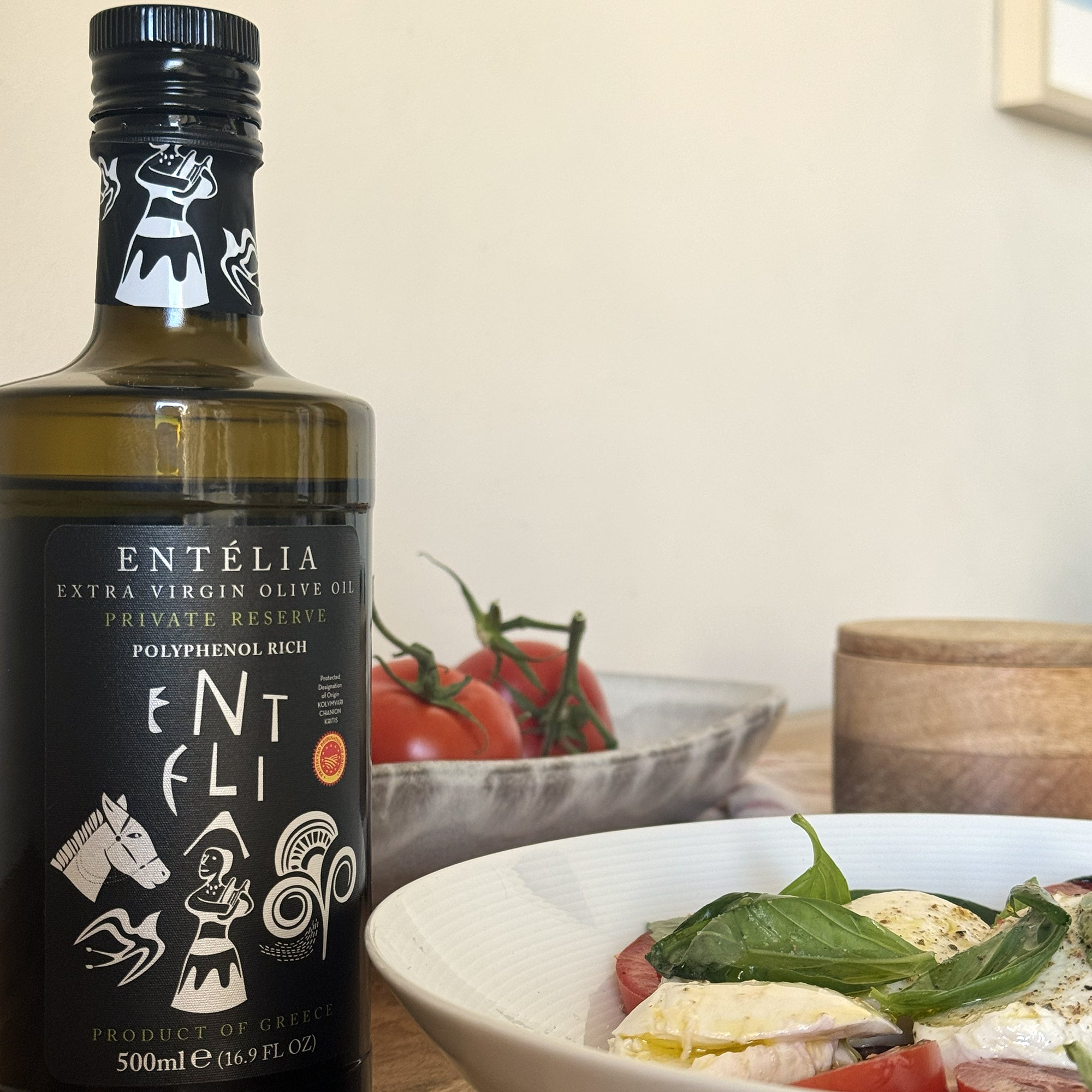 Entelia Private Reserve olive oil bottle beside a tomato, mozzarella, and basil salad.