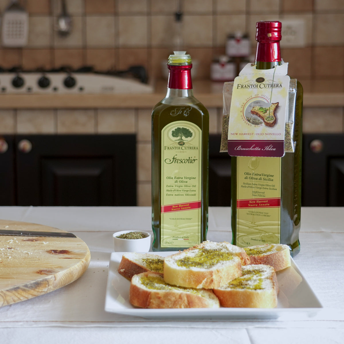Frescolio Novello 500ml bottles with seasoned bruschetta slices in a kitchen.