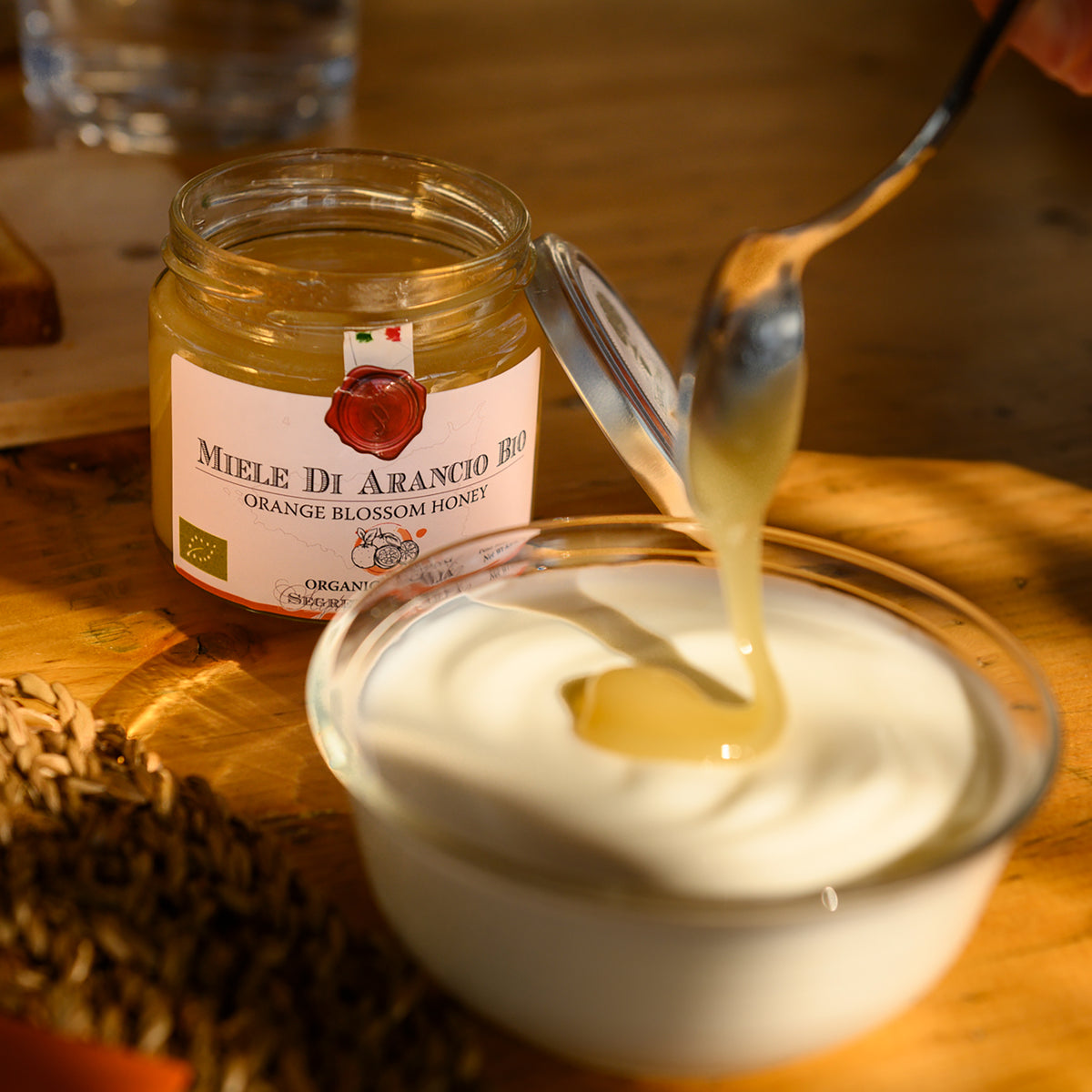 Frantoi Cutrera Organic Orange Blossom Honey being drizzled from a spoon into a bowl of yogurt.