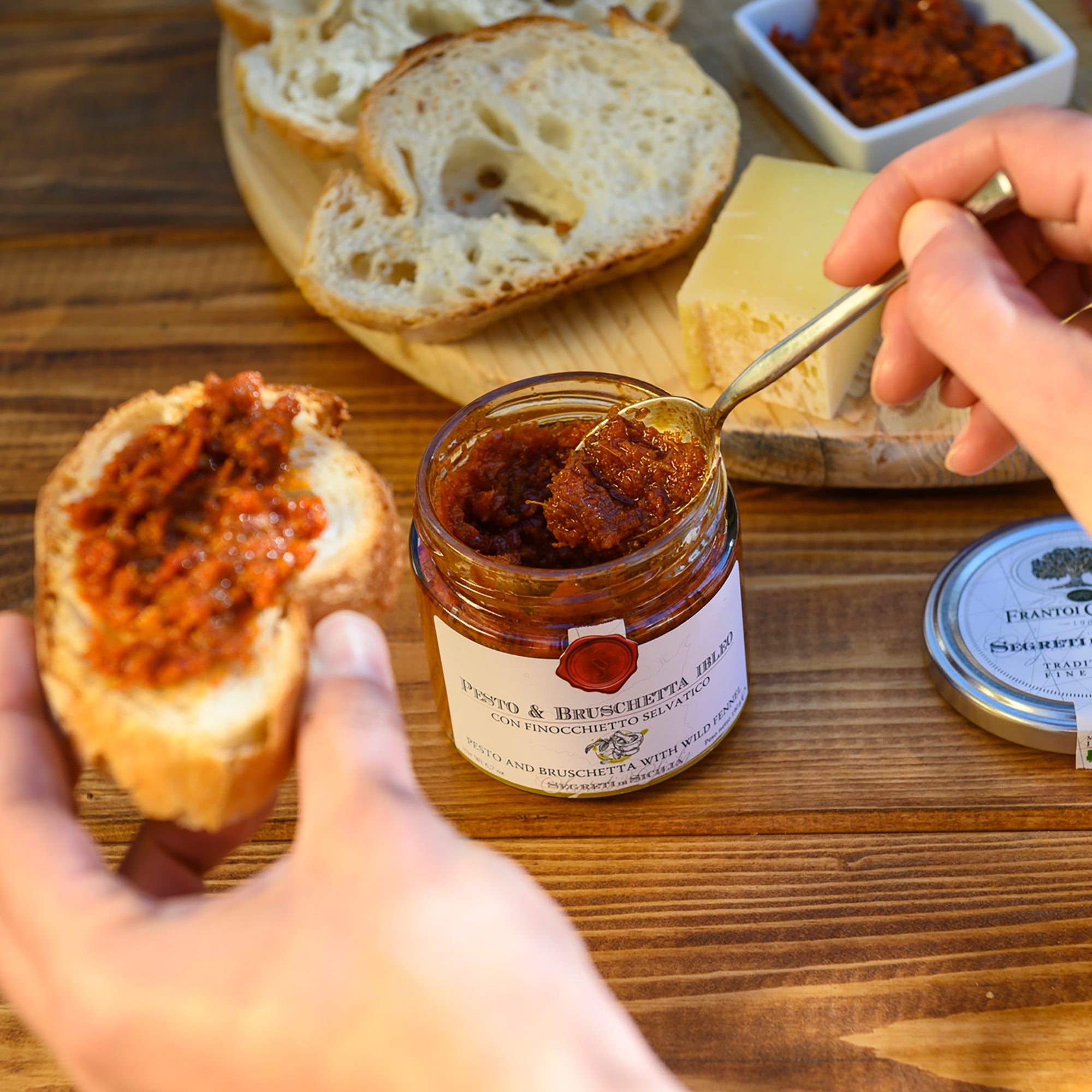 Spreading Frantoi Cutrera Pesto and Bruschetta onto sliced bread.