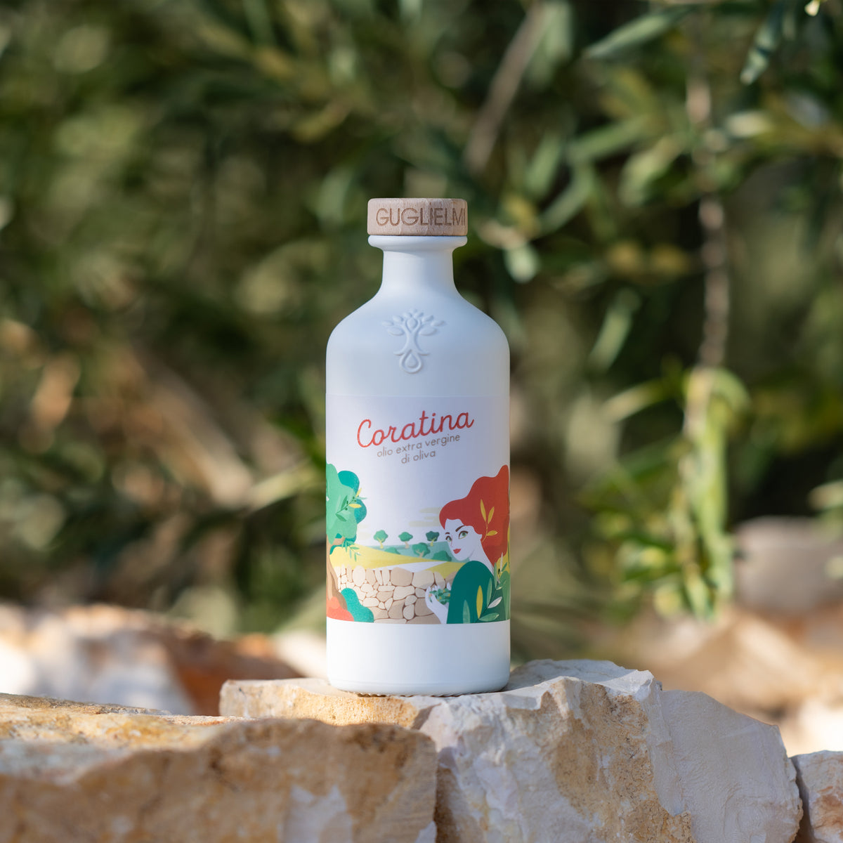 Guglielmi Le Monocultivar Coratina 500ml olive oil bottle on pale stone blocks in an olive grove.