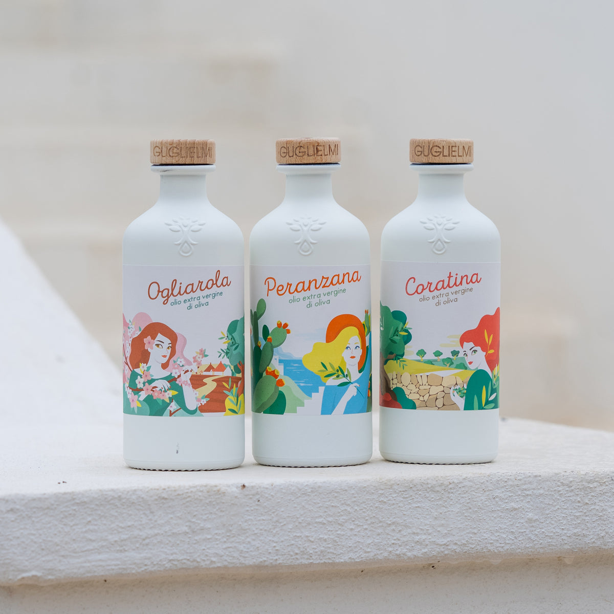 Guglielmi Ogliarola, Peranzana, and Coratina extra virgin olive oil bottles on a stone ledge.