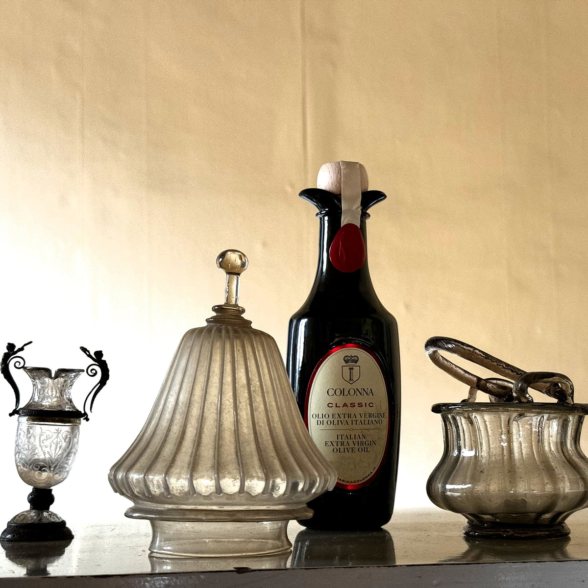 750 ml bottle of Colonna Classic extra virgin olive oil among antique glass and vessels.